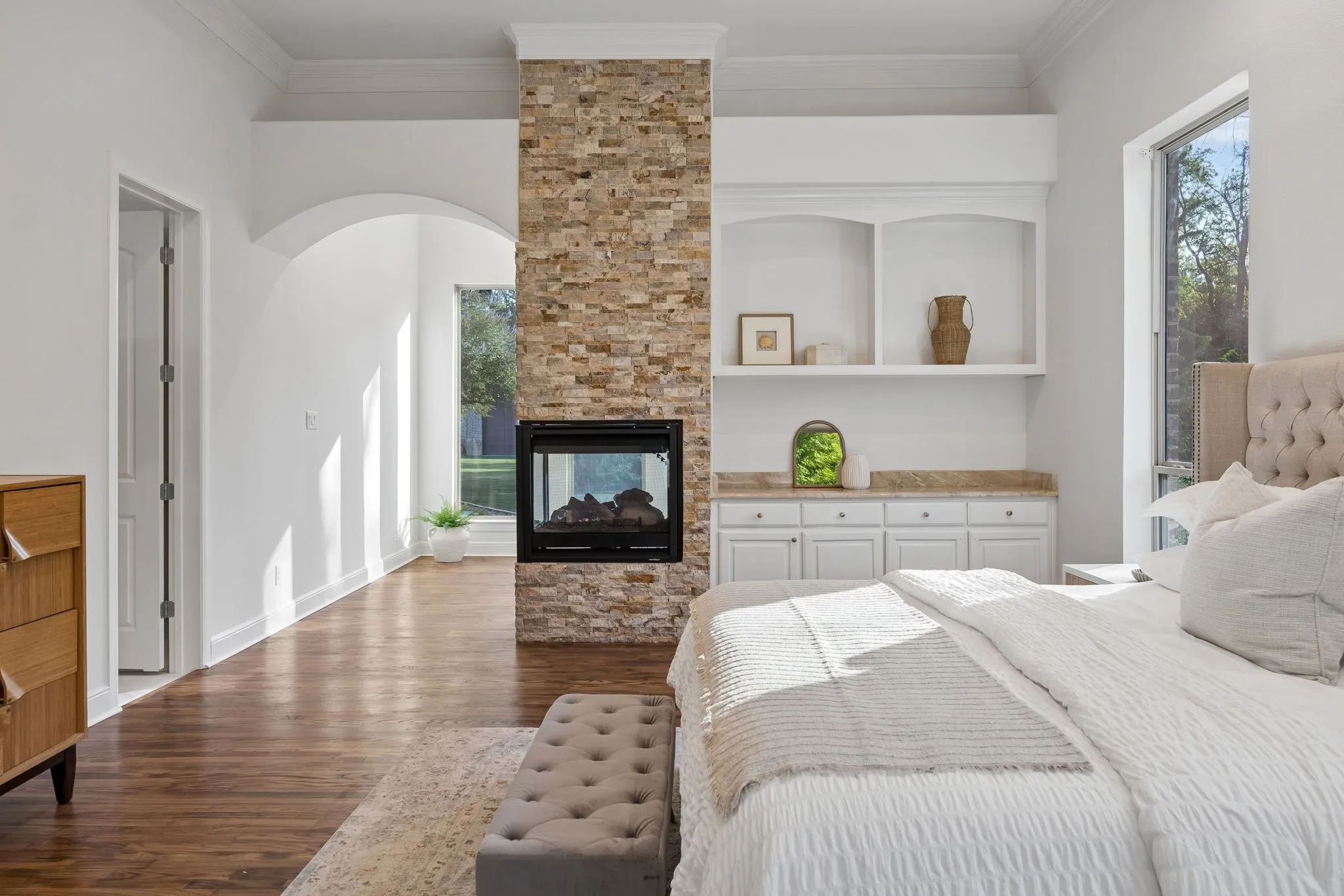 Stone-clad fireplace with a built-in electric insert, wood-finish flooring, arched entryway, and white built-in cabinetry with a stone countertop