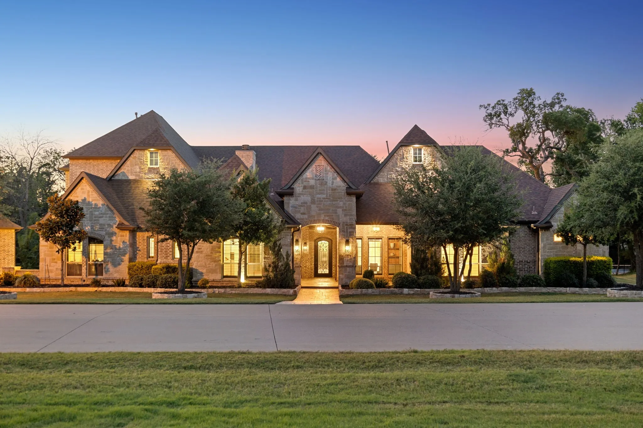 Stone and brick exterior residence featuring a prominent gabled roofline, dormer window, and mature front landscaping