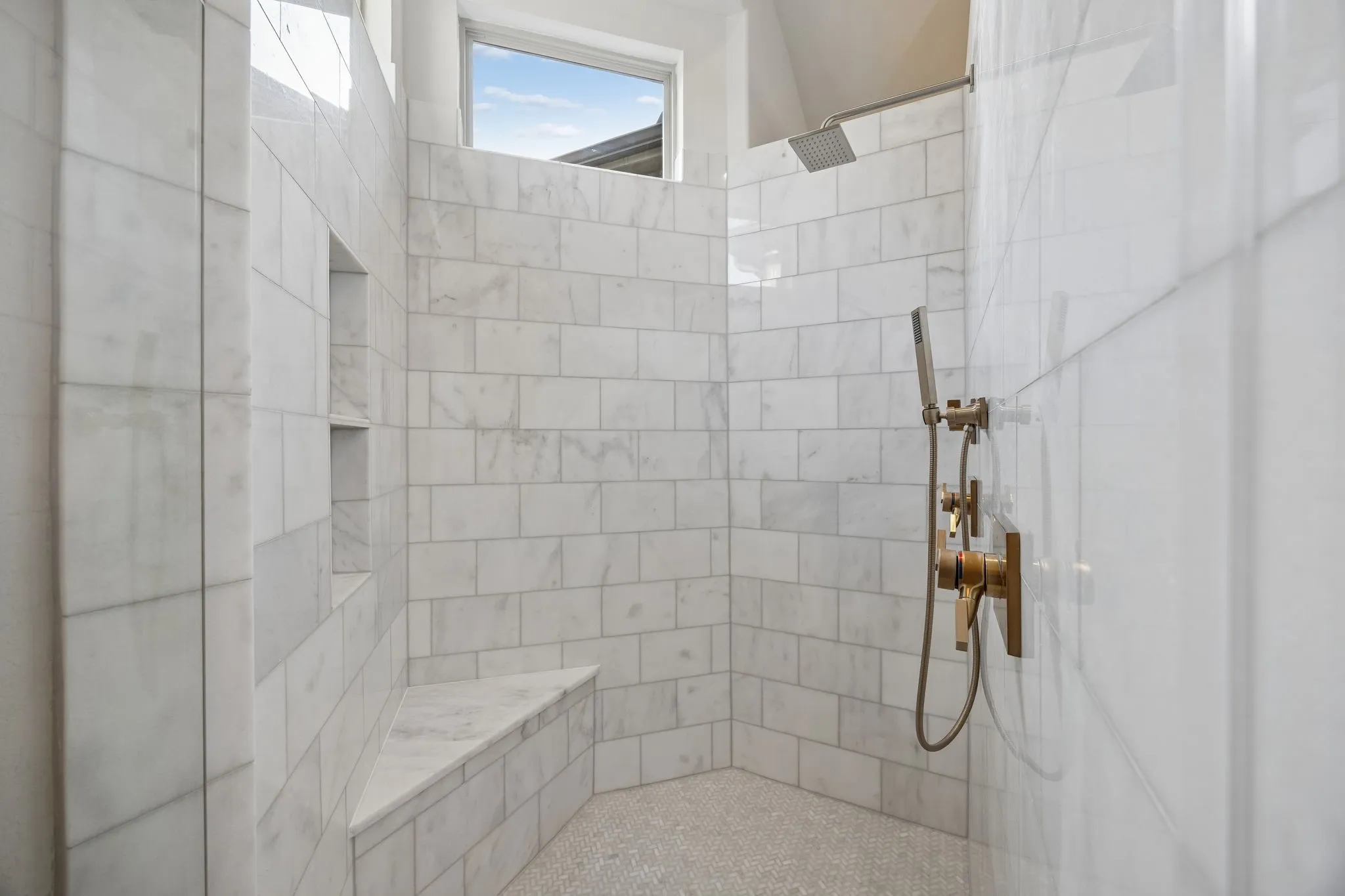 Walk-in shower featuring subway tile walls, a built-in bench, recessed shelving, a rain shower head, and a handheld shower fixture