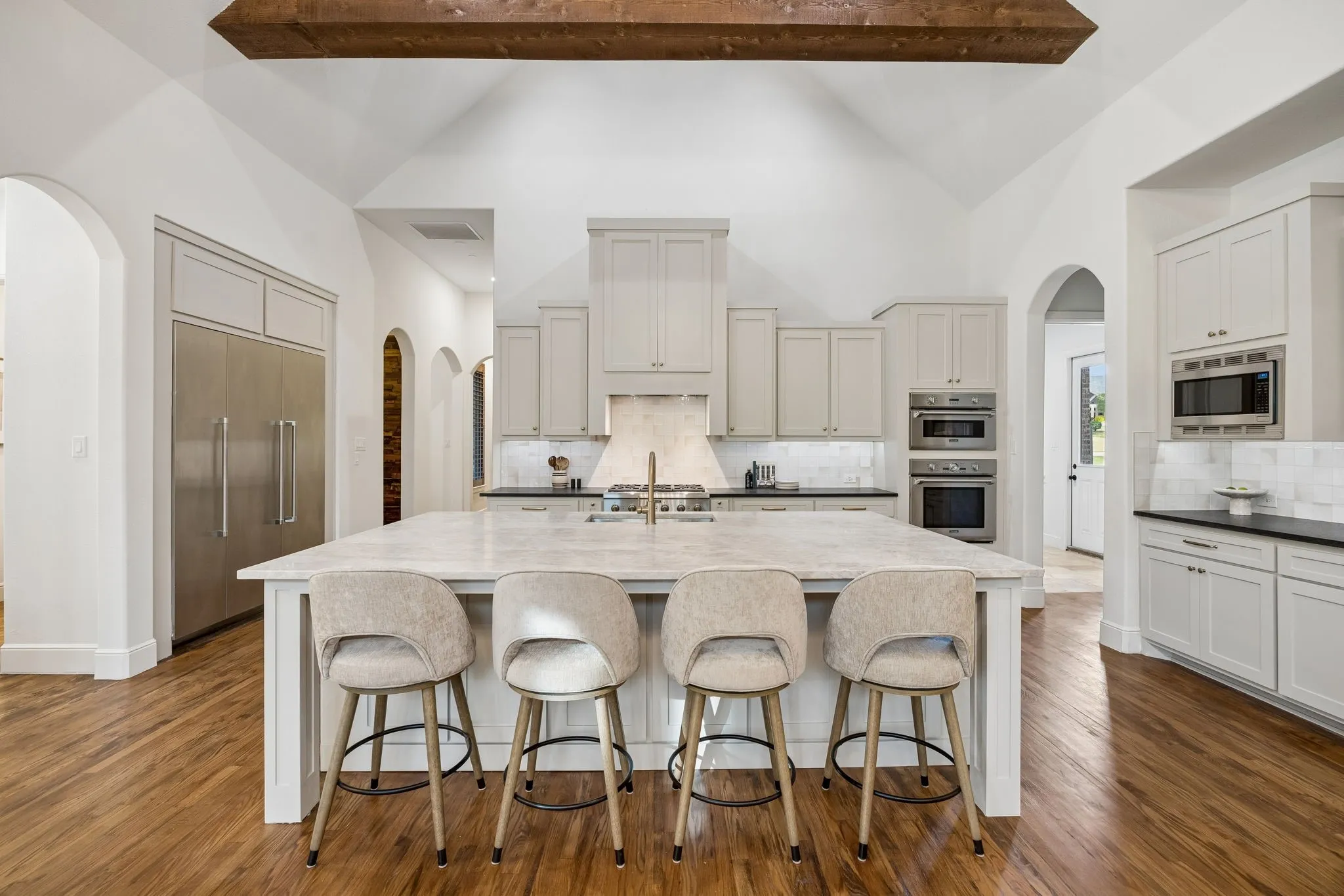 Kitchen featuring a large central island with seating, vaulted ceilings with a wood beam, stainless steel appliances, light cabinetry, and wood-finish flooring
