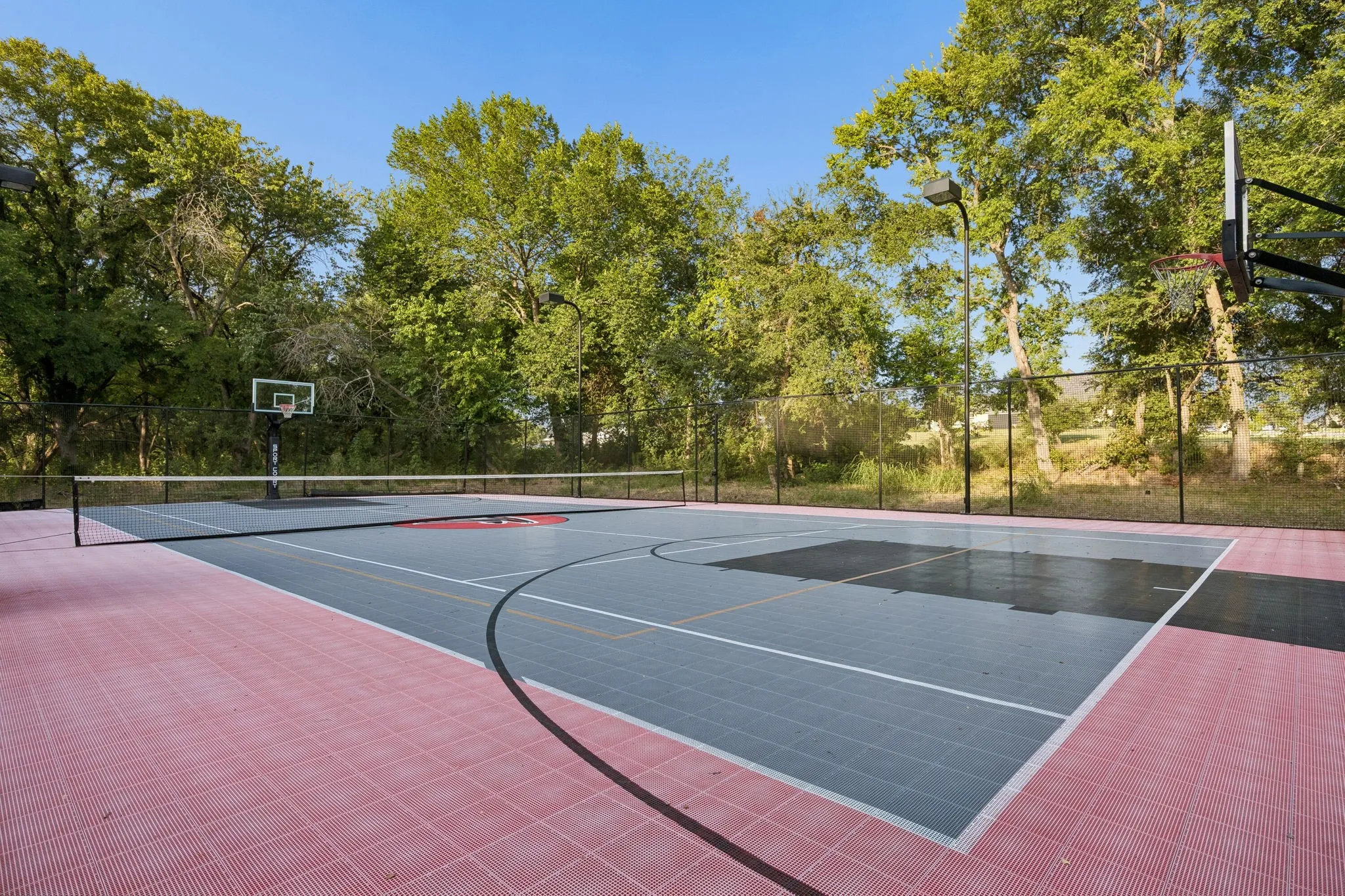 Multi-sport court featuring a modular tile surface in red and gray, basketball hoops, and a tennis net