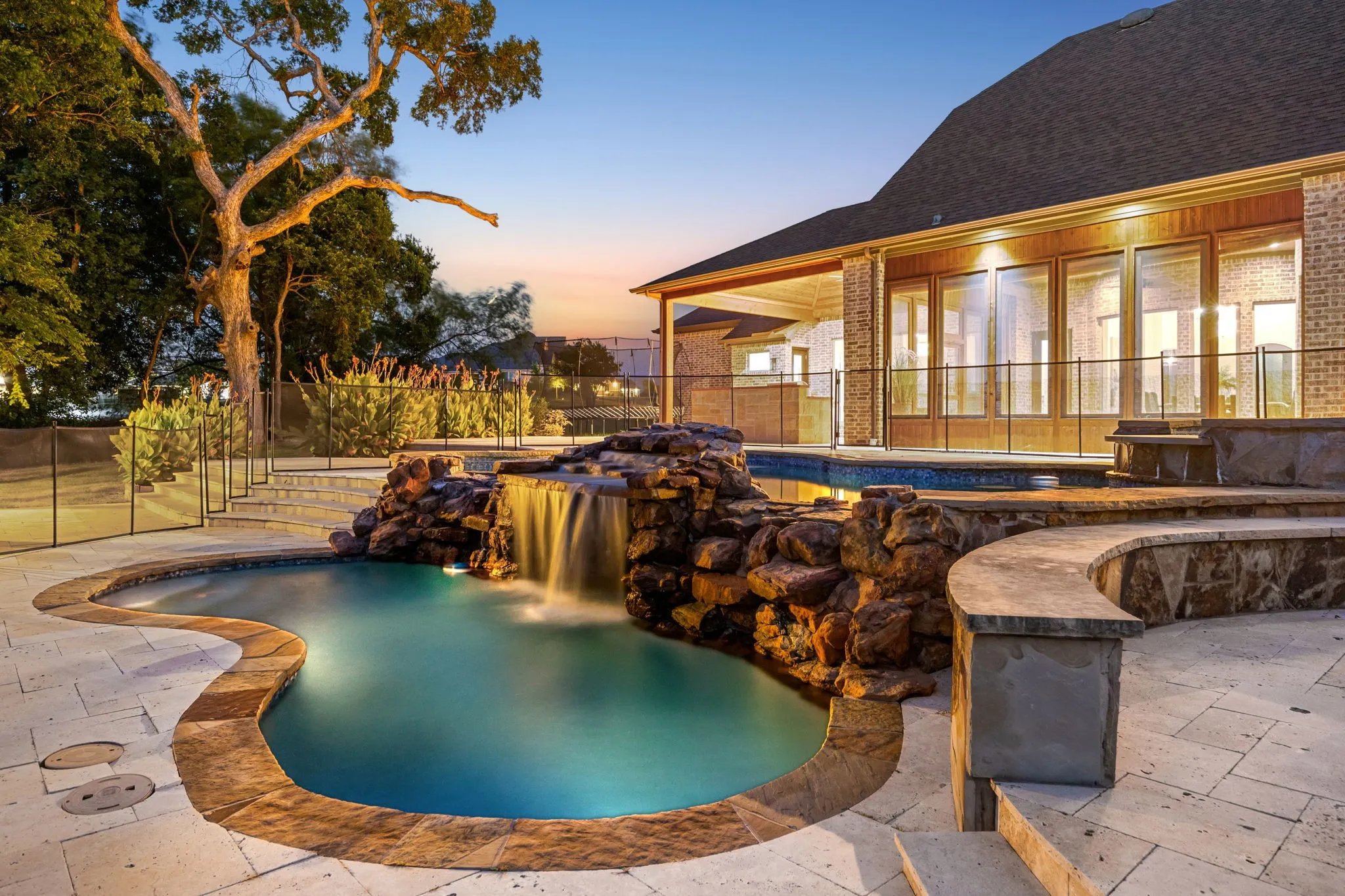 Freeform swimming pool with rock waterfall feature, stone coping, and paved patio surround
