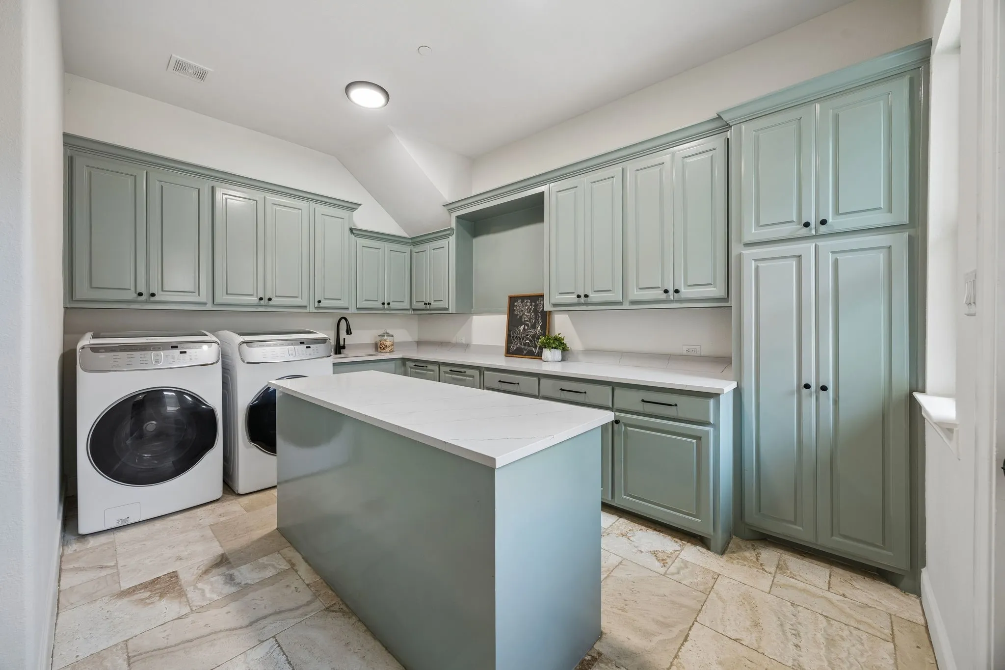 Laundry room featuring extensive light green cabinetry, white countertops, a central island with a white countertop, and patterned tile flooring
