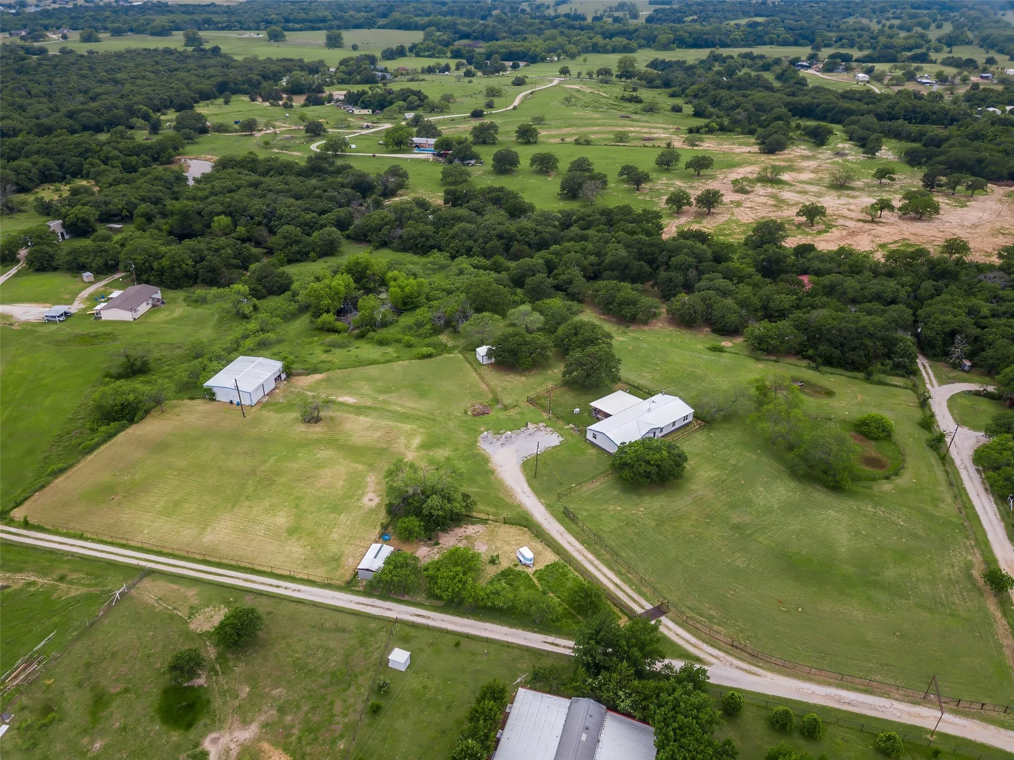 Expansive rural landscape featuring multiple structures, including a primary residence with a white exterior and a metal roof, and a large metal outbuilding