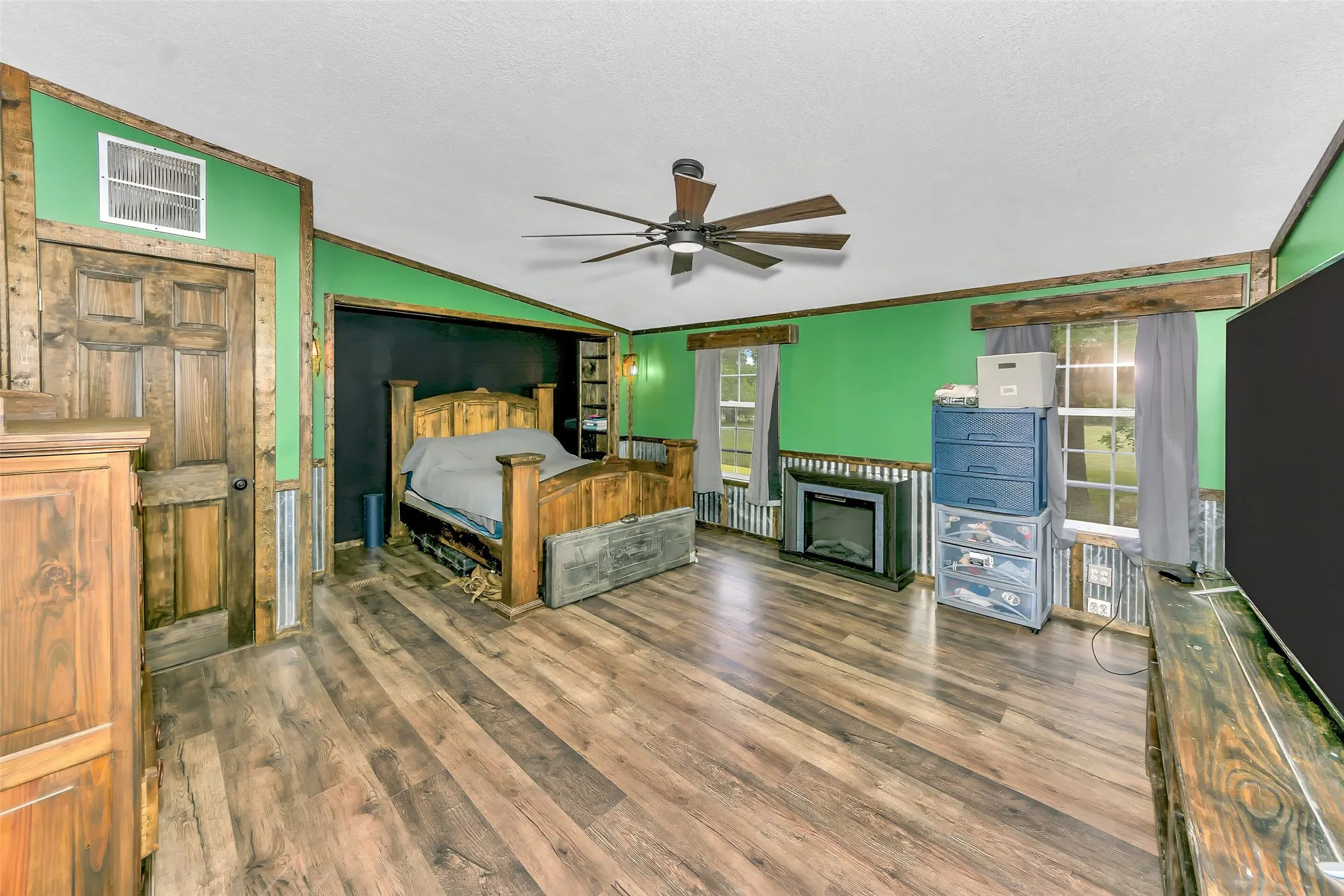 Spacious room featuring wood-finish flooring, a ceiling fan, and vibrant green walls with wood trim