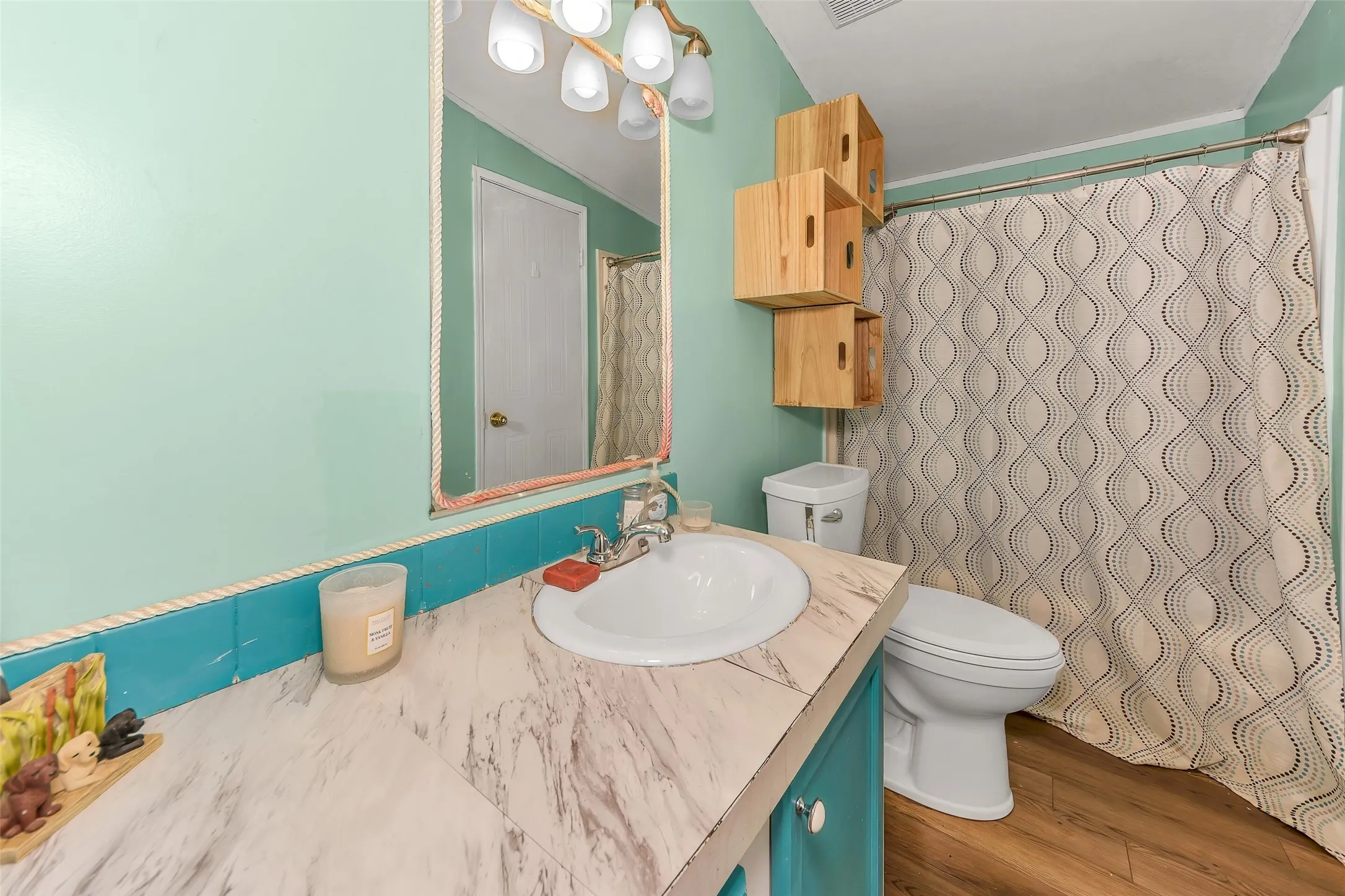 Bathroom featuring wood-finish flooring, a vanity with a white countertop and integrated sink, a wall-mounted mirror, and decorative wall-mounted wooden storage cubes