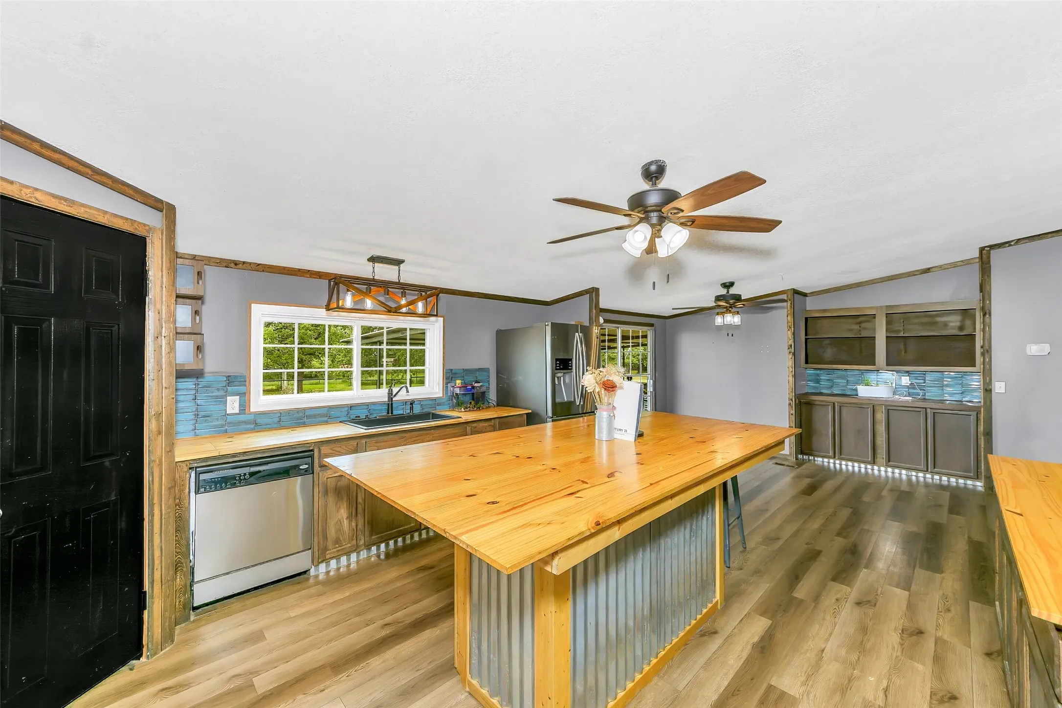 Kitchen featuring a wood-top island with corrugated metal base, stainless steel appliances, wood-finish flooring, and a window above the sink
