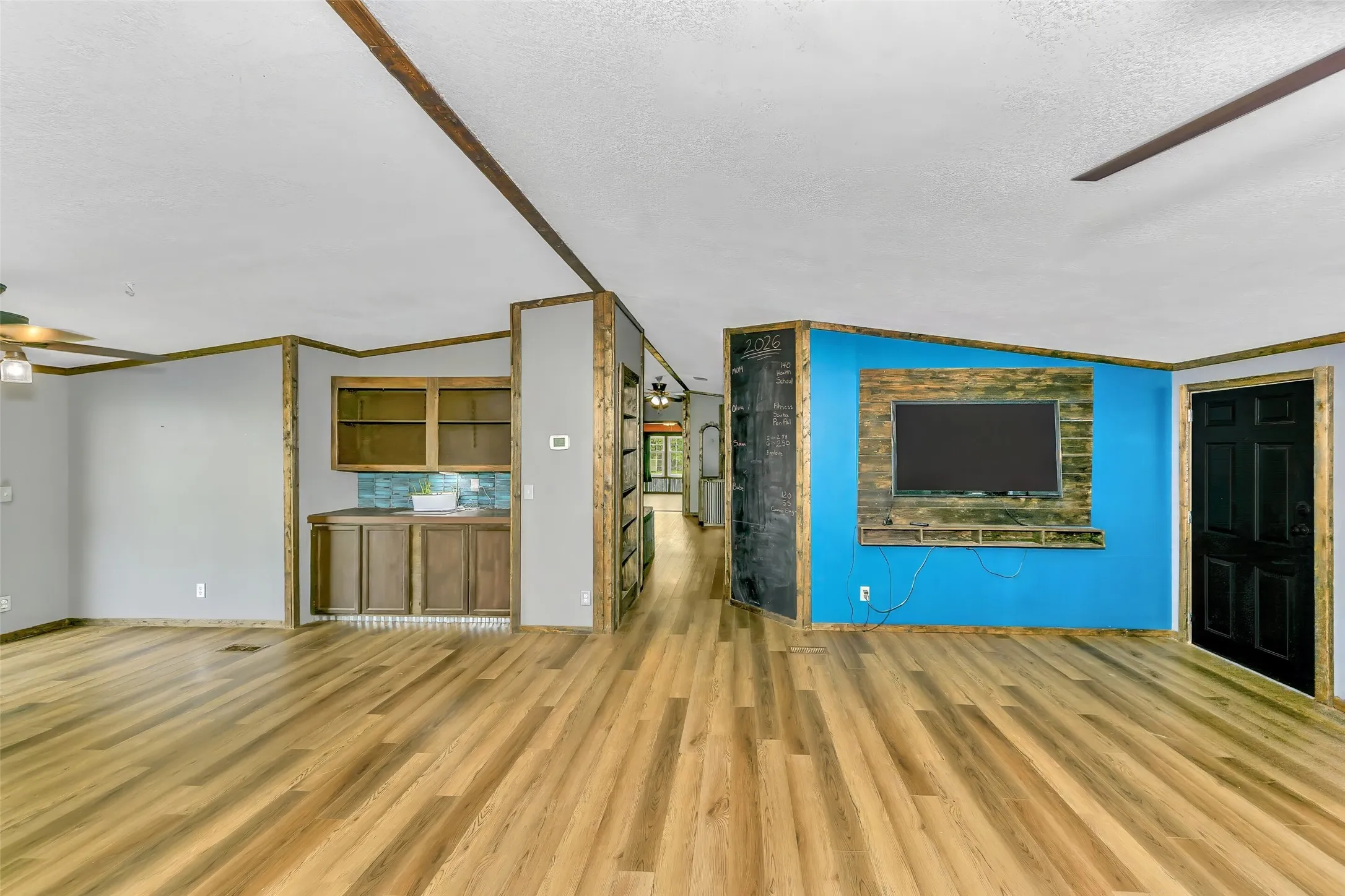 Open concept living area featuring wood-finish flooring, a built-in wet bar with cabinetry and tile backsplash, and a media wall with wood paneling