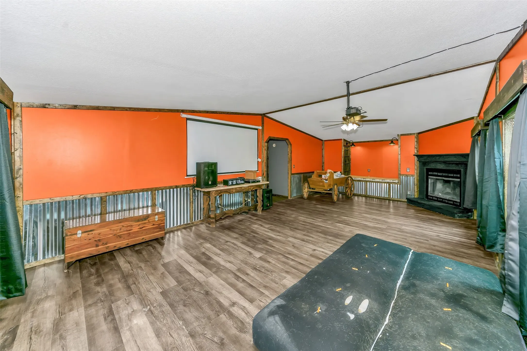 Spacious room featuring wood-finish flooring, a ceiling fan, and a fireplace with a dark surround