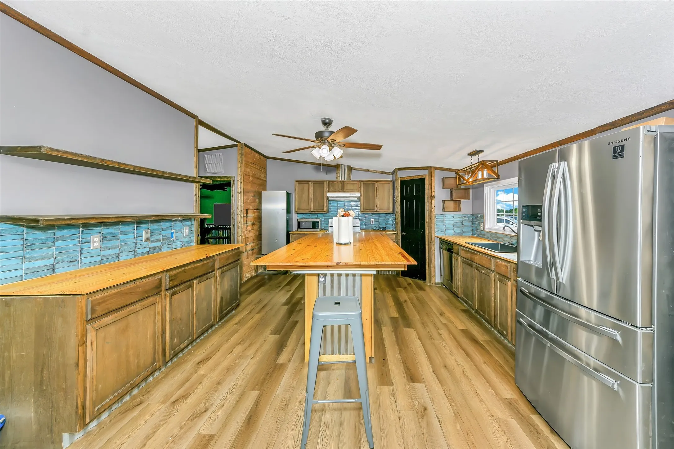 Spacious kitchen featuring a central island with wood countertop, wood-finish flooring, and ample wood cabinetry