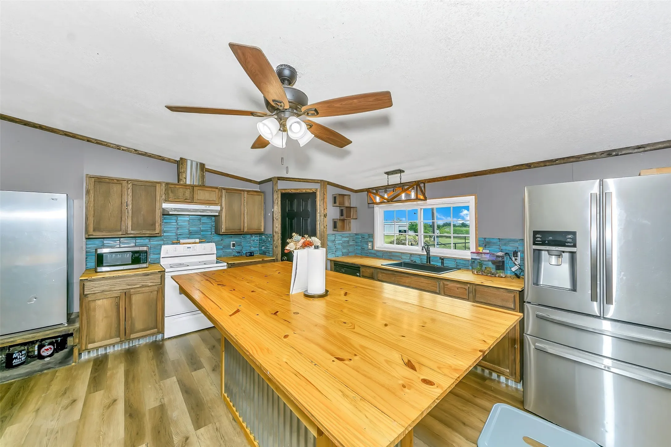 Spacious kitchen featuring a large wood-finish island with corrugated metal accents, wood-finish flooring, and light wood cabinetry