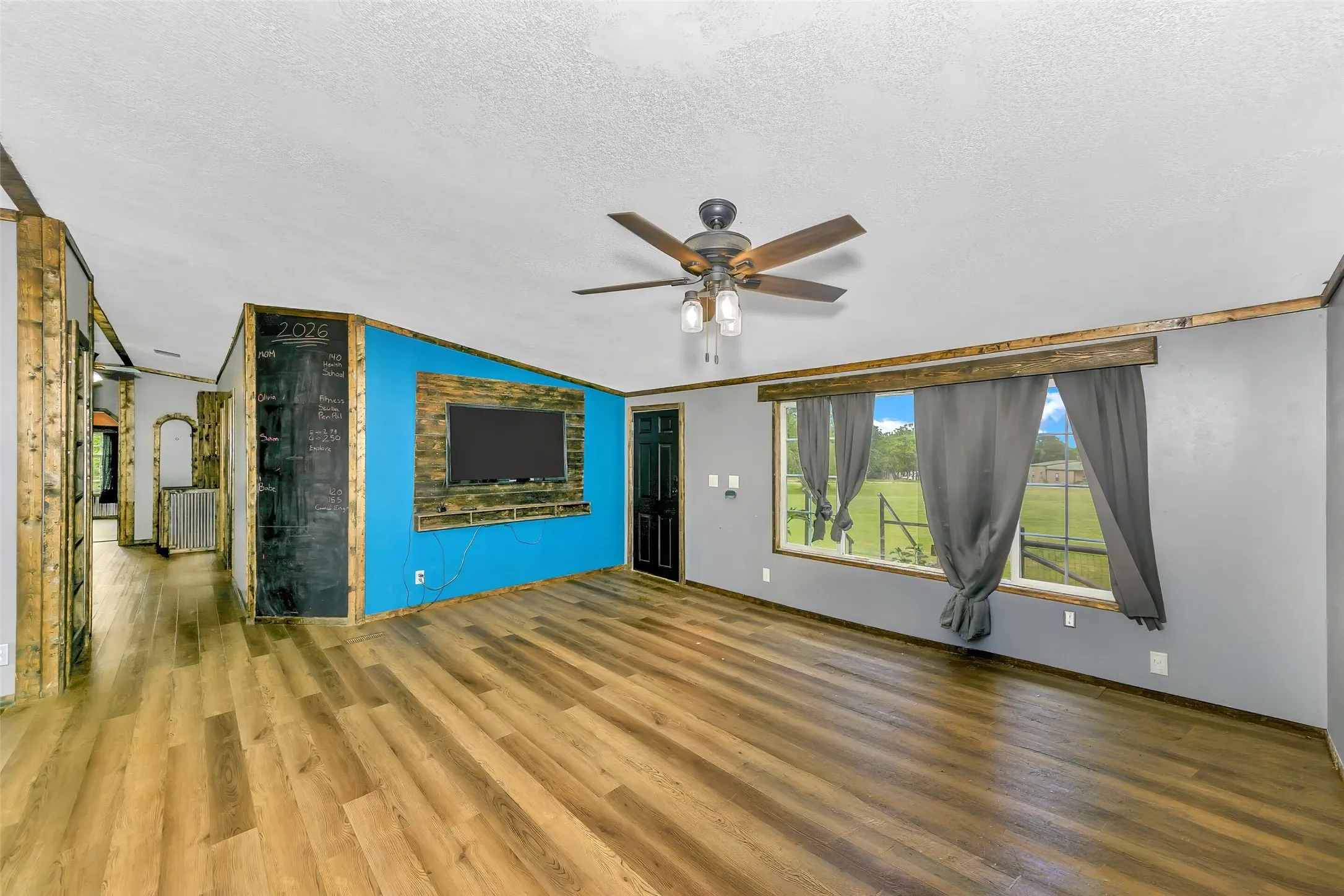 Spacious interior featuring wood-finish flooring, a ceiling fan, and a wall-mounted chalkboard accent-AI removal of furniture