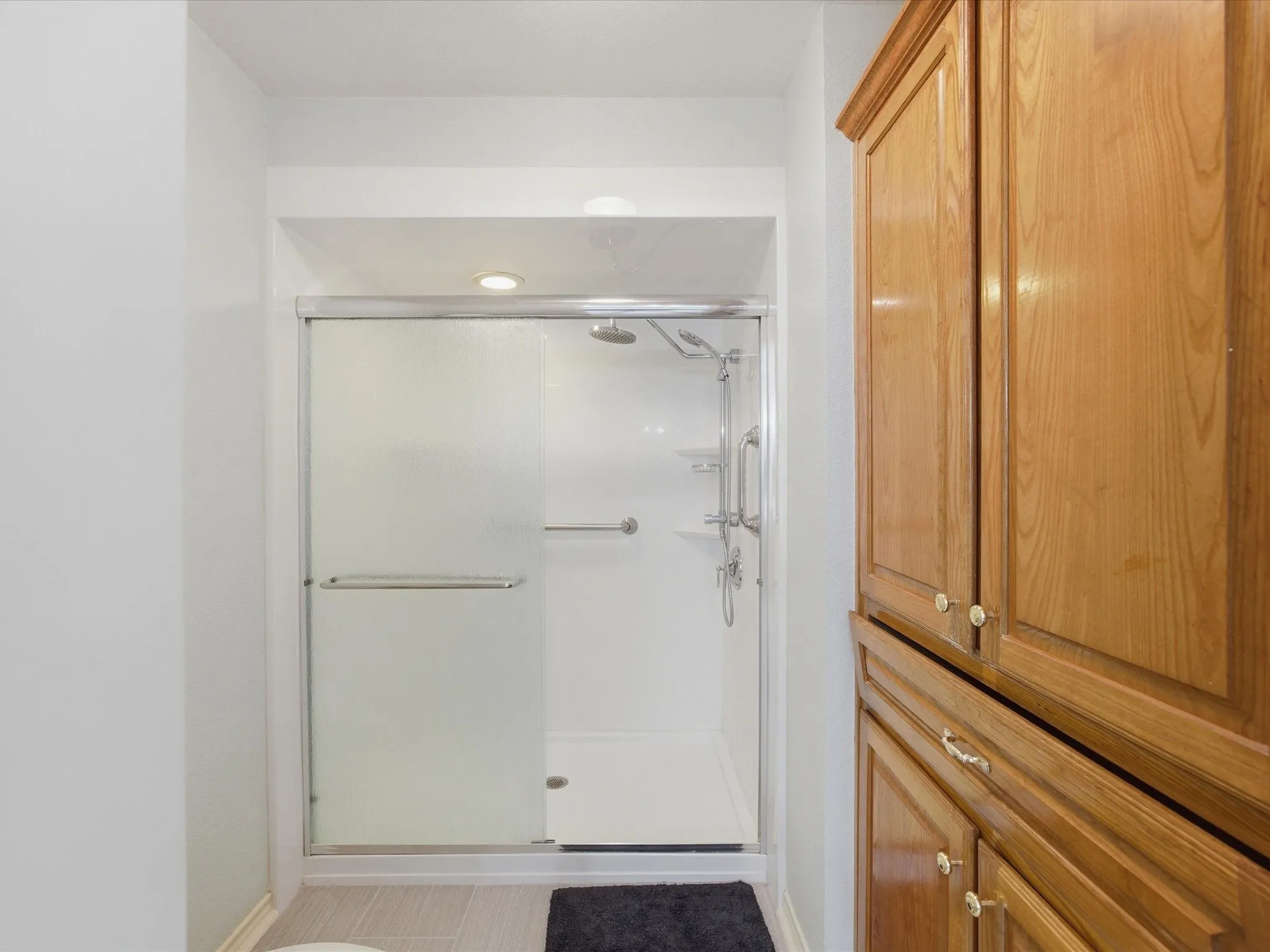 Primary en-suite bath featuring separate shower with rain shower head, shower attachment, built-in cabinetry and commode
