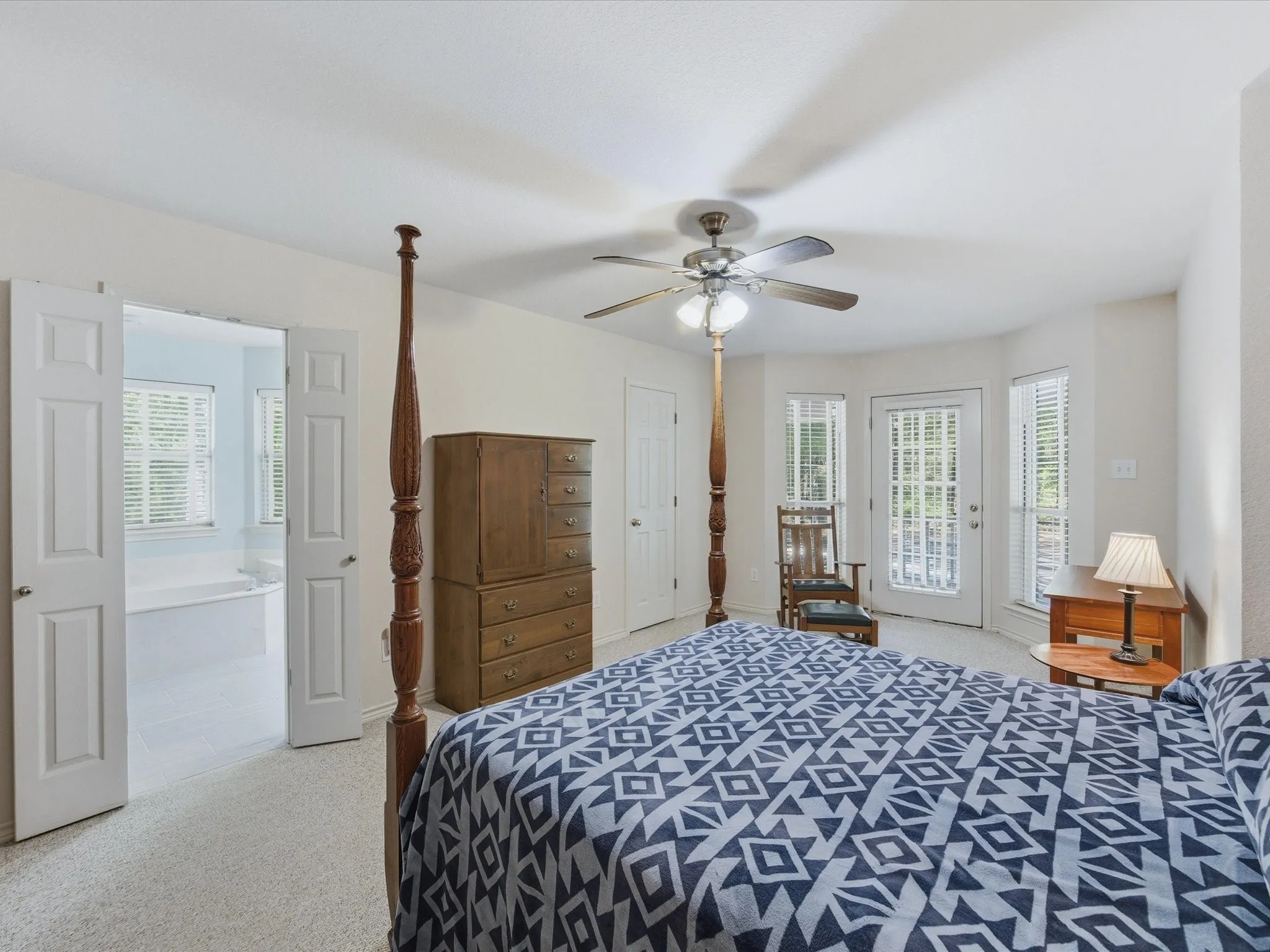 Large primary bedroom with ceiling fan and walk-in closet and private door to back porch with window coverings.