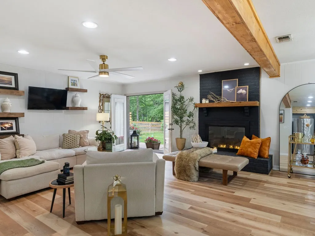 Spacious living area featuring wood-finish flooring, a black brick fireplace with a wood mantle, and exposed ceiling beams
