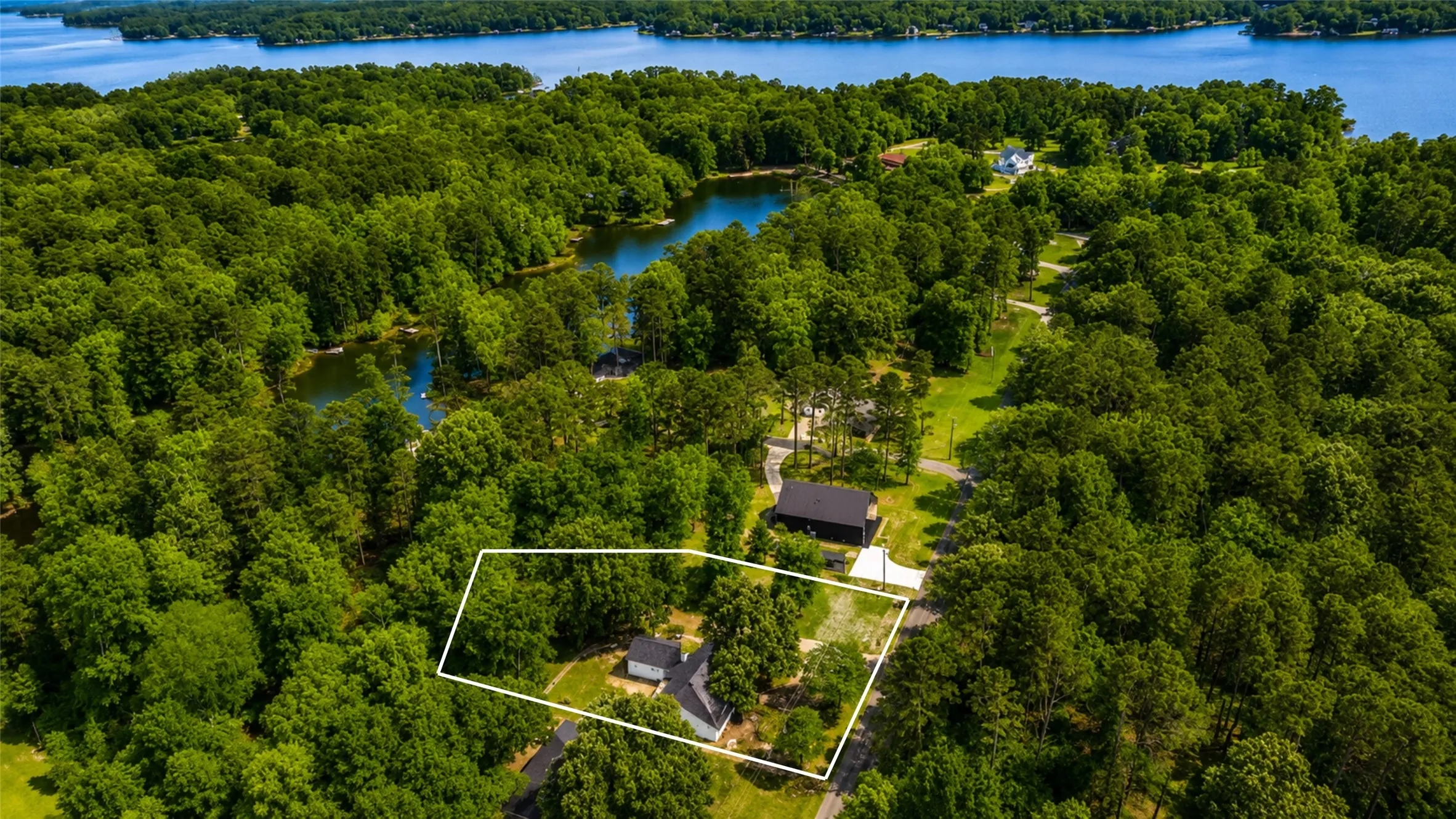Expansive wooded property featuring a lake and two ponds, with a partial clearing and a visible single-story residence