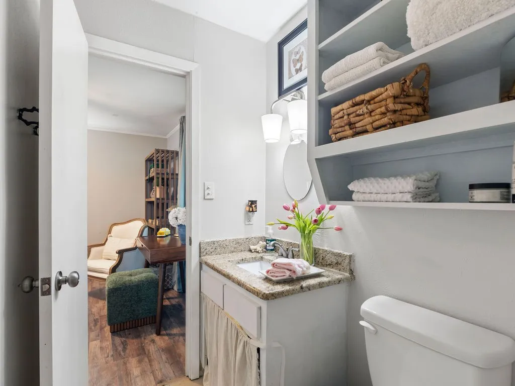 Bathroom vanity featuring a granite countertop with an undermount sink, built-in shelving, and a toilet