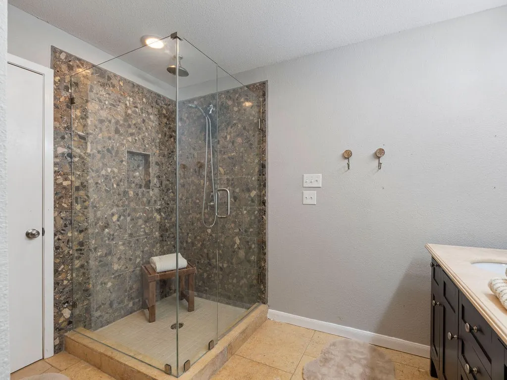 Walk-in shower featuring glass enclosure, stone-finish tile, recessed niche, and a rain showerhead