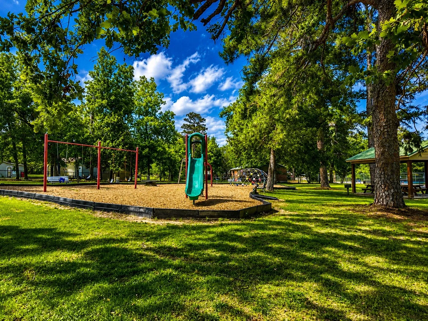 Outdoor recreation area featuring a playground with a slide, swing set, and geodesic dome climber