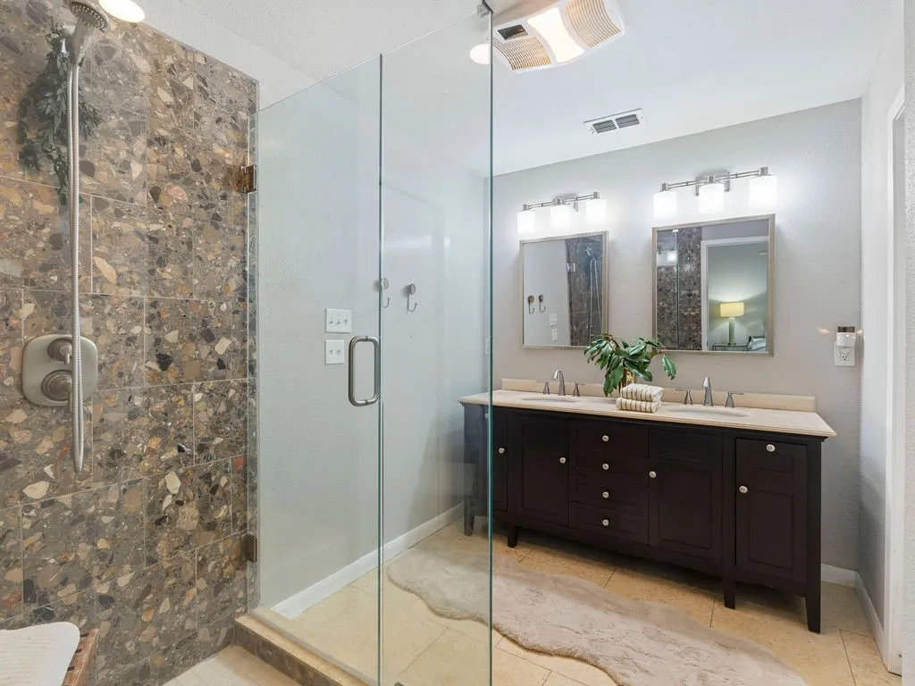 Glass-enclosed shower with full-height stone-look tile surround and a built-in shower bench