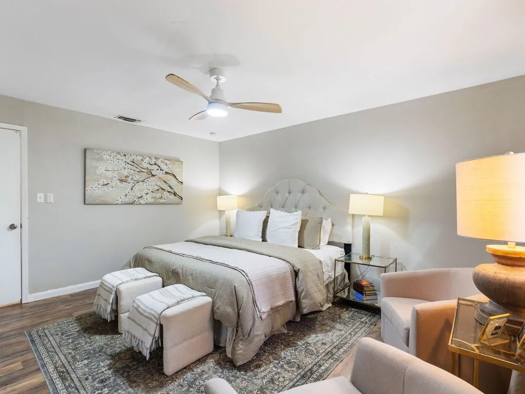 Bedroom featuring wood-finish flooring, a ceiling fan with integrated lighting, a tufted upholstered headboard, and a built-in closet with a solid white door