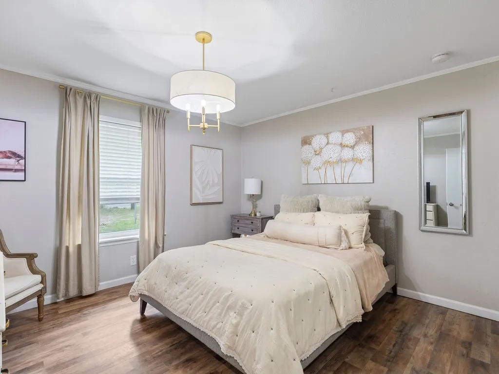 Spacious room featuring wood-finish flooring, a window with horizontal blinds and drapes, a modern drum pendant light fixture, and a full-length wall mirror