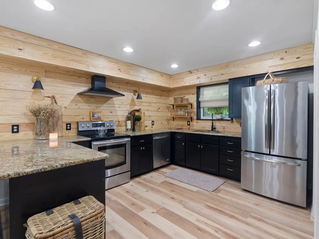 Kitchen featuring wood plank walls, black cabinetry, granite countertops, stainless steel appliances, and recessed lighting