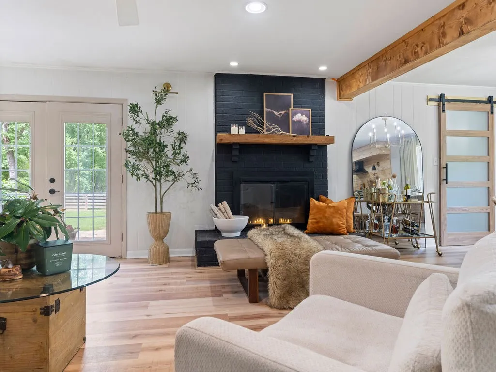 Living space featuring a black brick fireplace with a wood mantel, light wood-finish flooring, and exposed wood beam