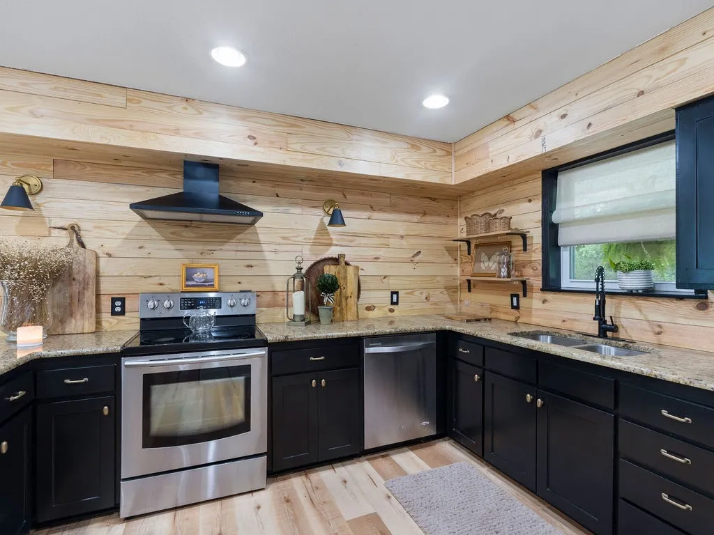 Kitchen featuring wood paneling, black cabinetry, stainless steel appliances, granite-look countertops, and recessed lighting
