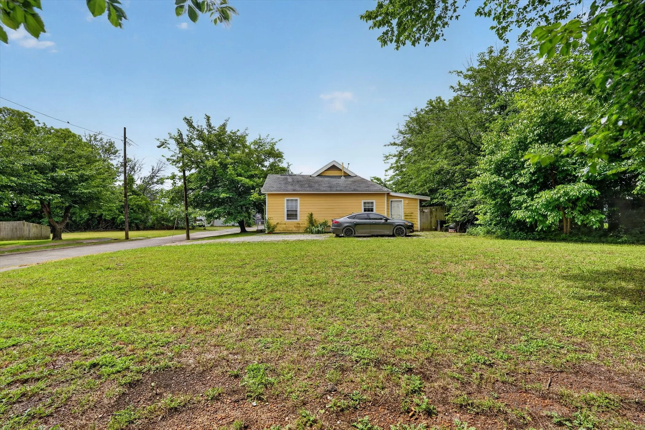 Expansive grassy yard with mature trees and a paved driveway leading to a yellow-sided residence