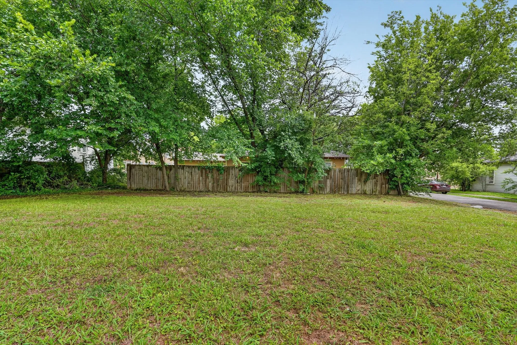 Expansive green lawn with mature trees and a wood privacy fence