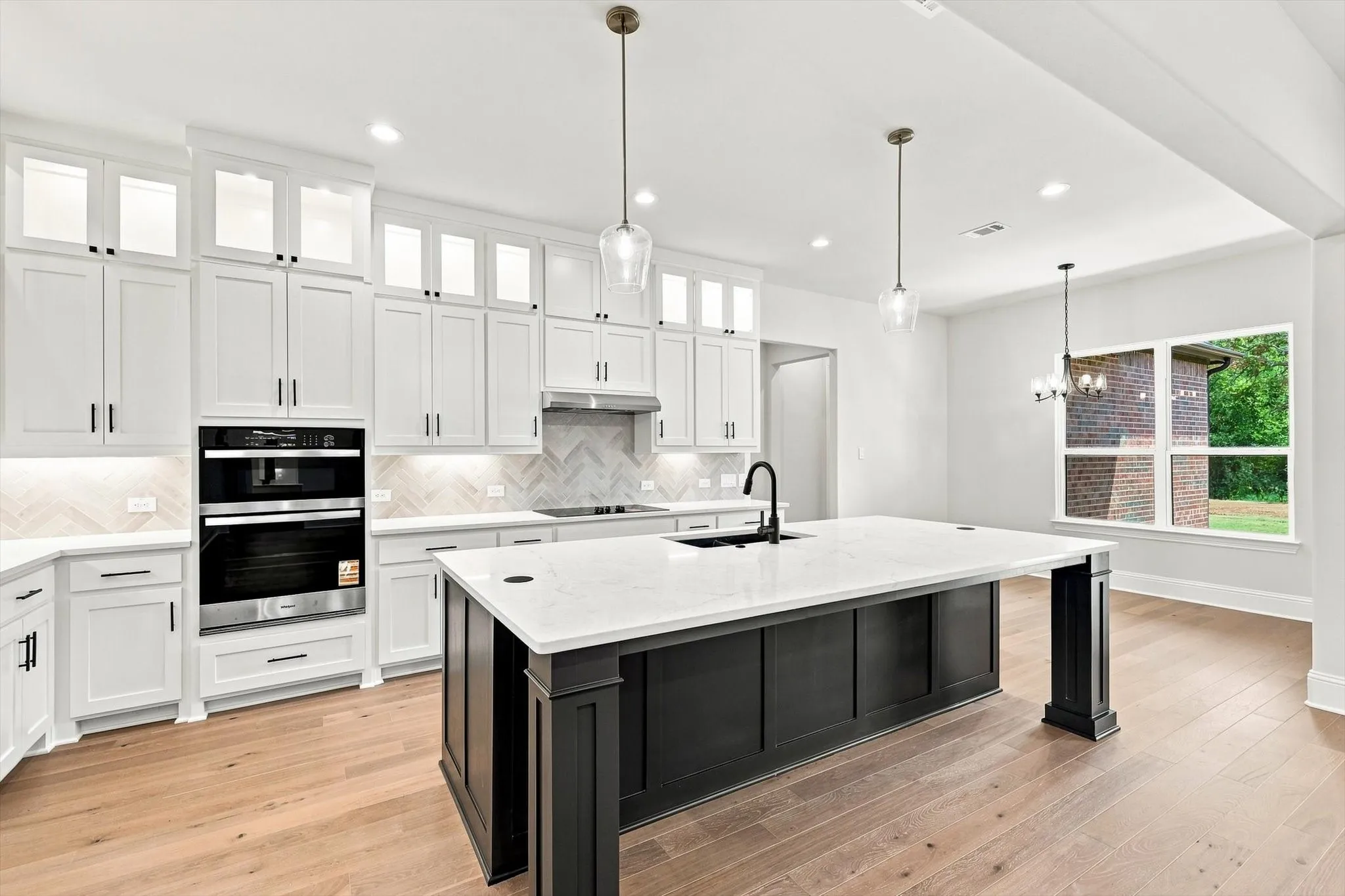White cabinetry with glass-front uppers, herringbone tile backsplash, built-in stainless steel appliances, large kitchen island with white countertop, and wood-finish flooring