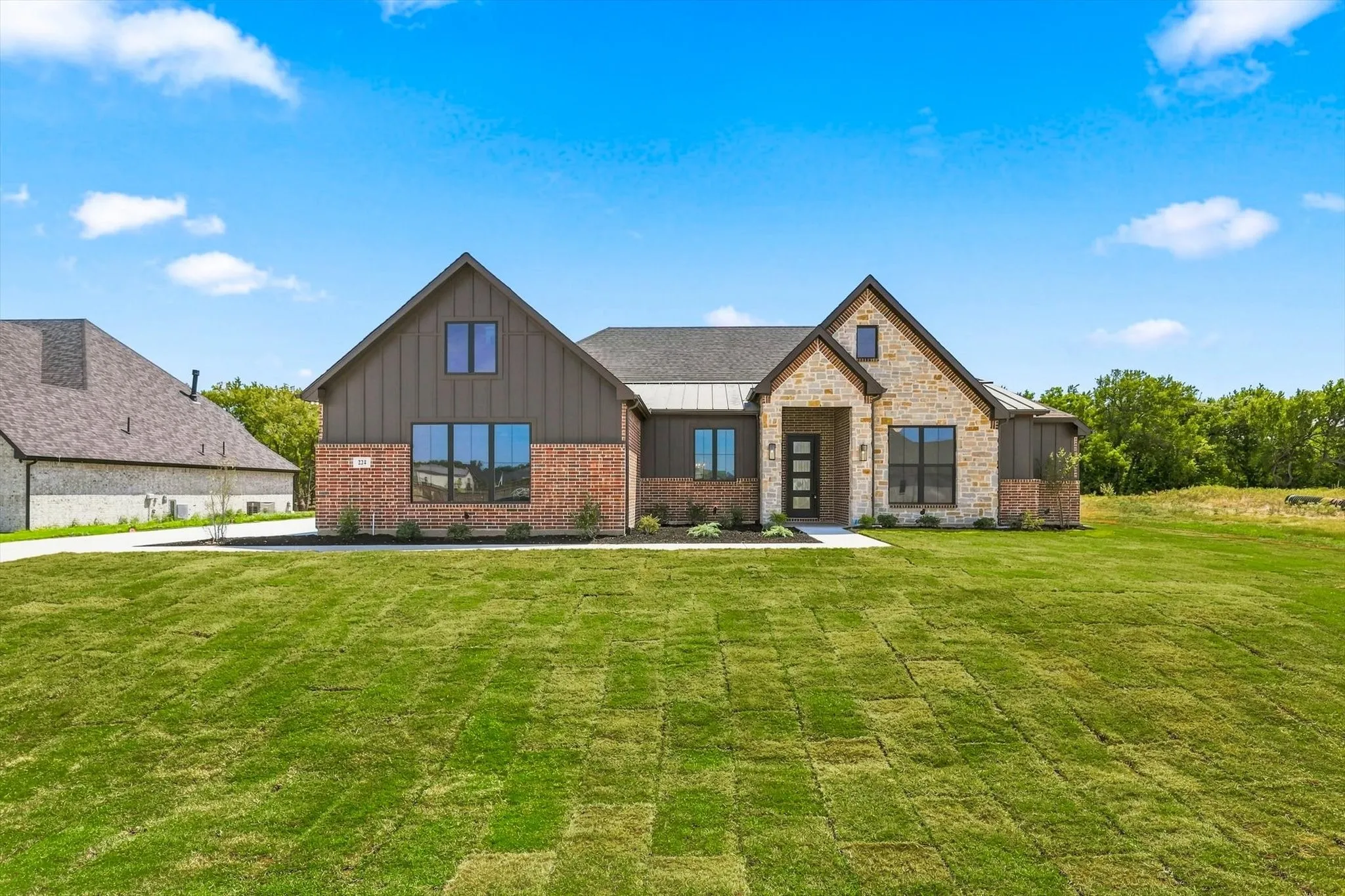 Modern farmhouse-style exterior featuring brick and stone masonry, board-and-batten siding, and a dark shingle roof