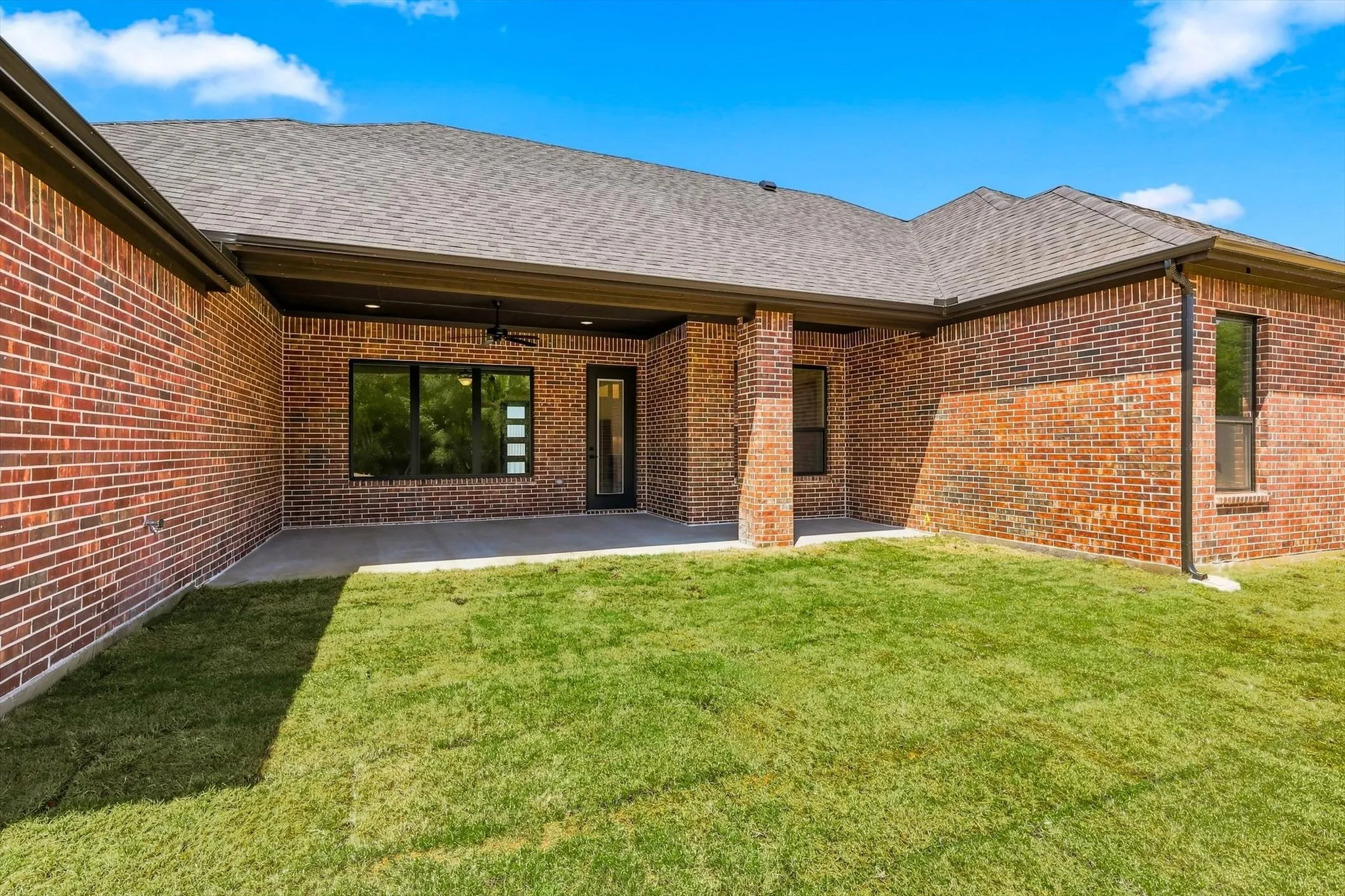 Brick exterior with a covered patio, concrete slab, and modern black window frames