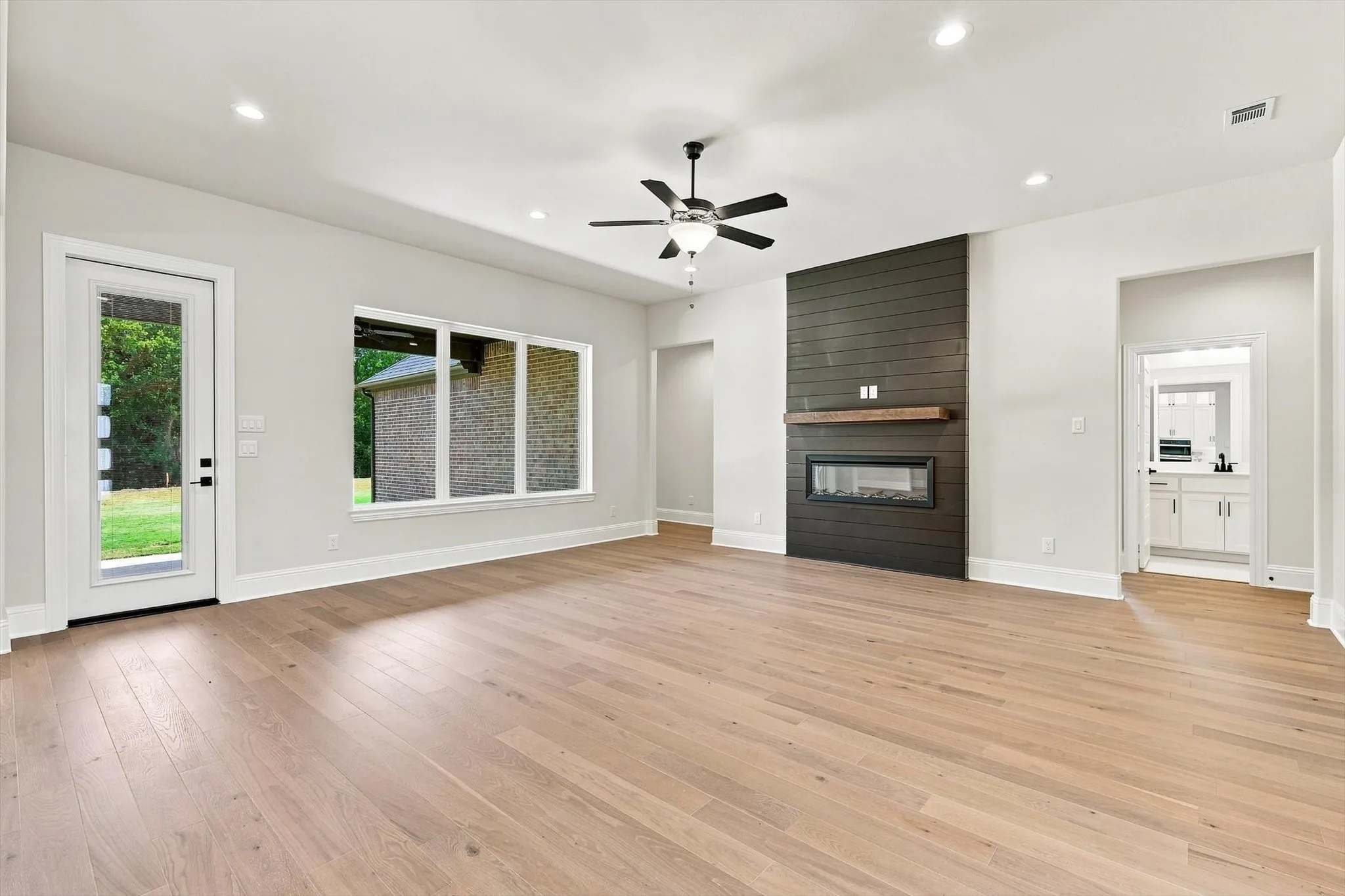 Wood-finish flooring throughout, featuring a linear fireplace with dark wood-paneled surround and wood mantel