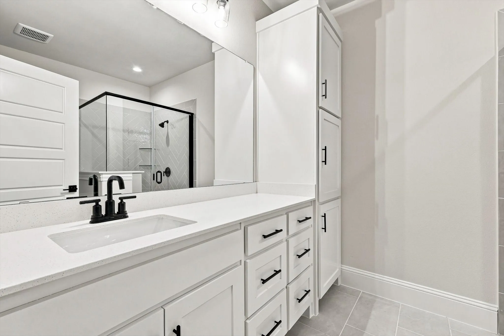 White vanity with a single integrated sink, stone-finish countertop, black hardware, and integrated storage tower
