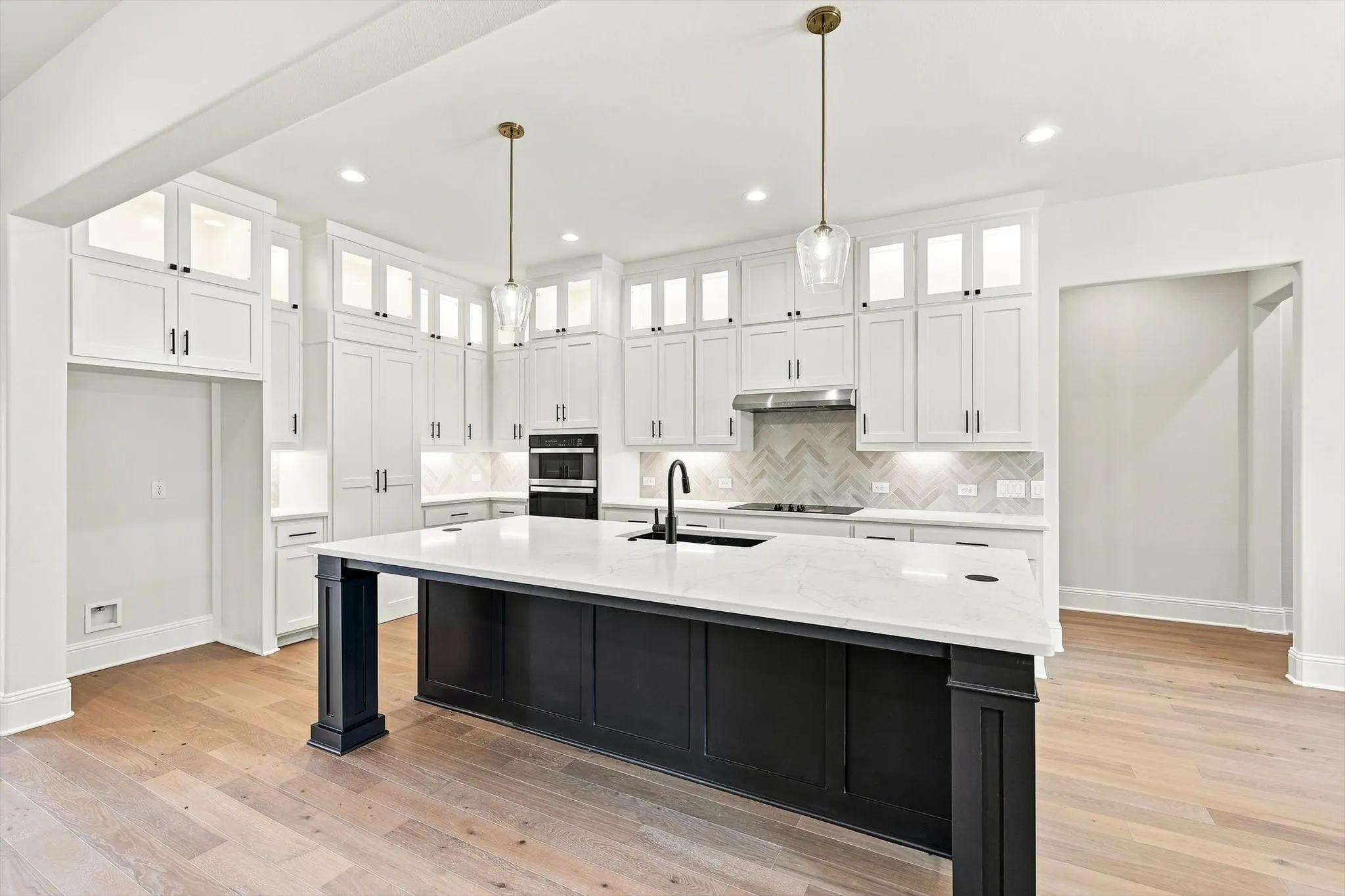 Gourmet kitchen featuring a large central island with seating, extensive white cabinetry, light wood-finish flooring, and dual wall ovens