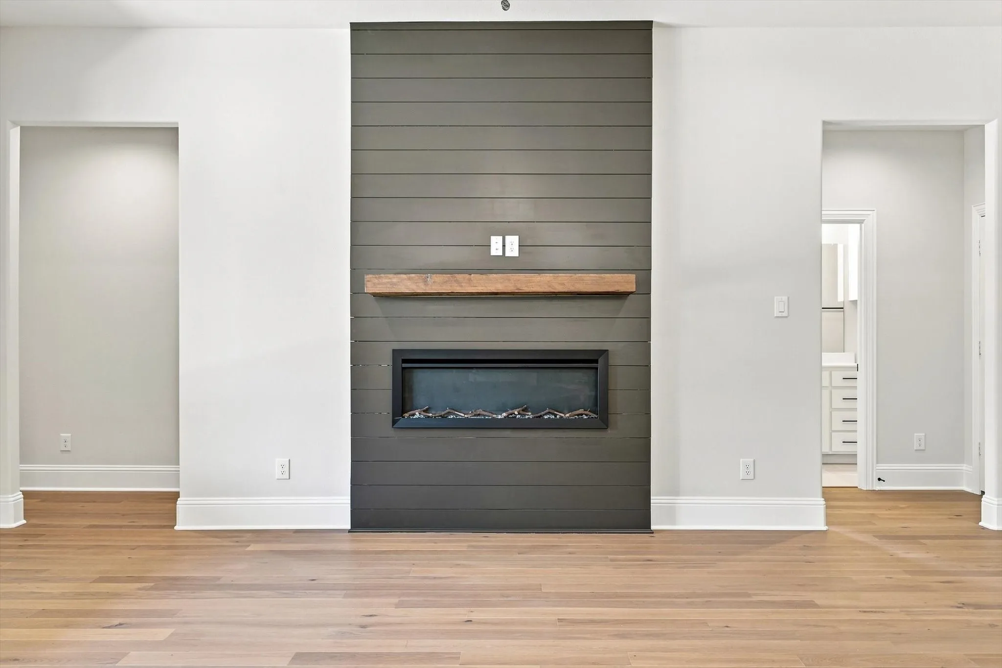 Hardwood flooring, shiplap accent wall, built-in electric fireplace, wood mantel, and crisp white trim