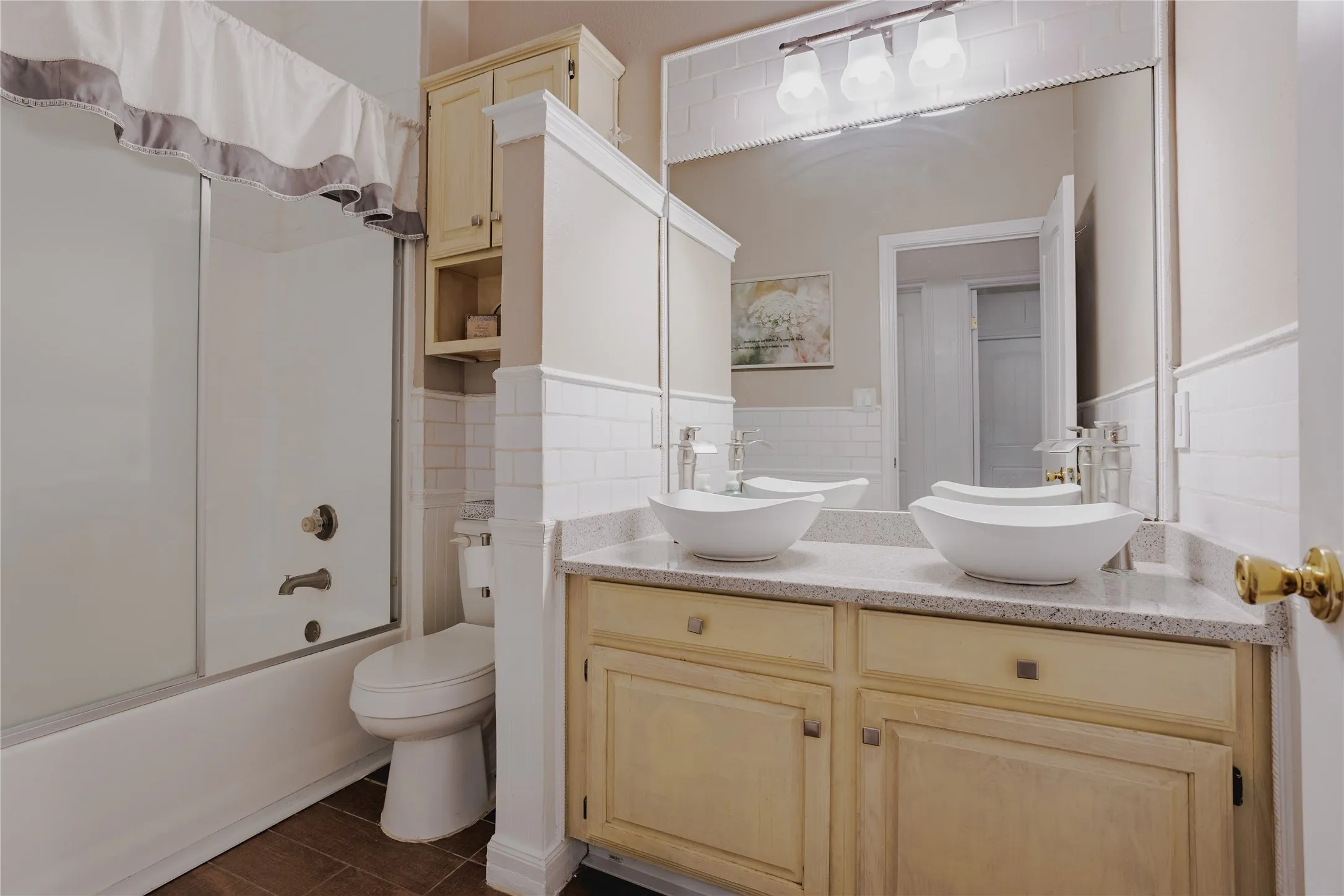 Dual-sink vanity with wood-finish cabinetry and stone countertops, paired with a large framed mirror and brass hardware