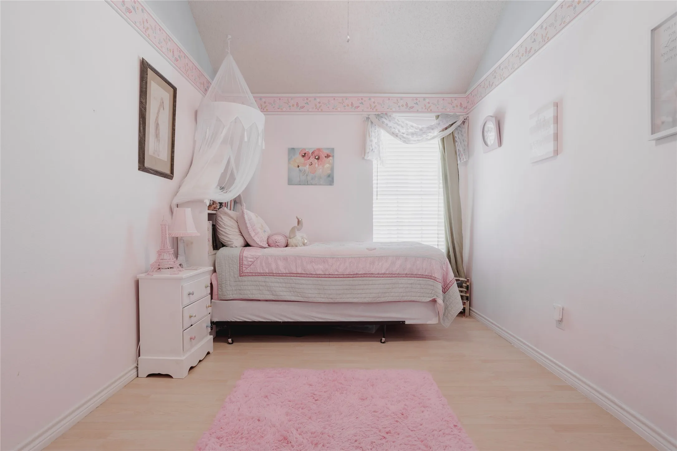 Vaulted ceiling, wood-finish flooring, window with blinds, decorative wall trim, built-in lighting