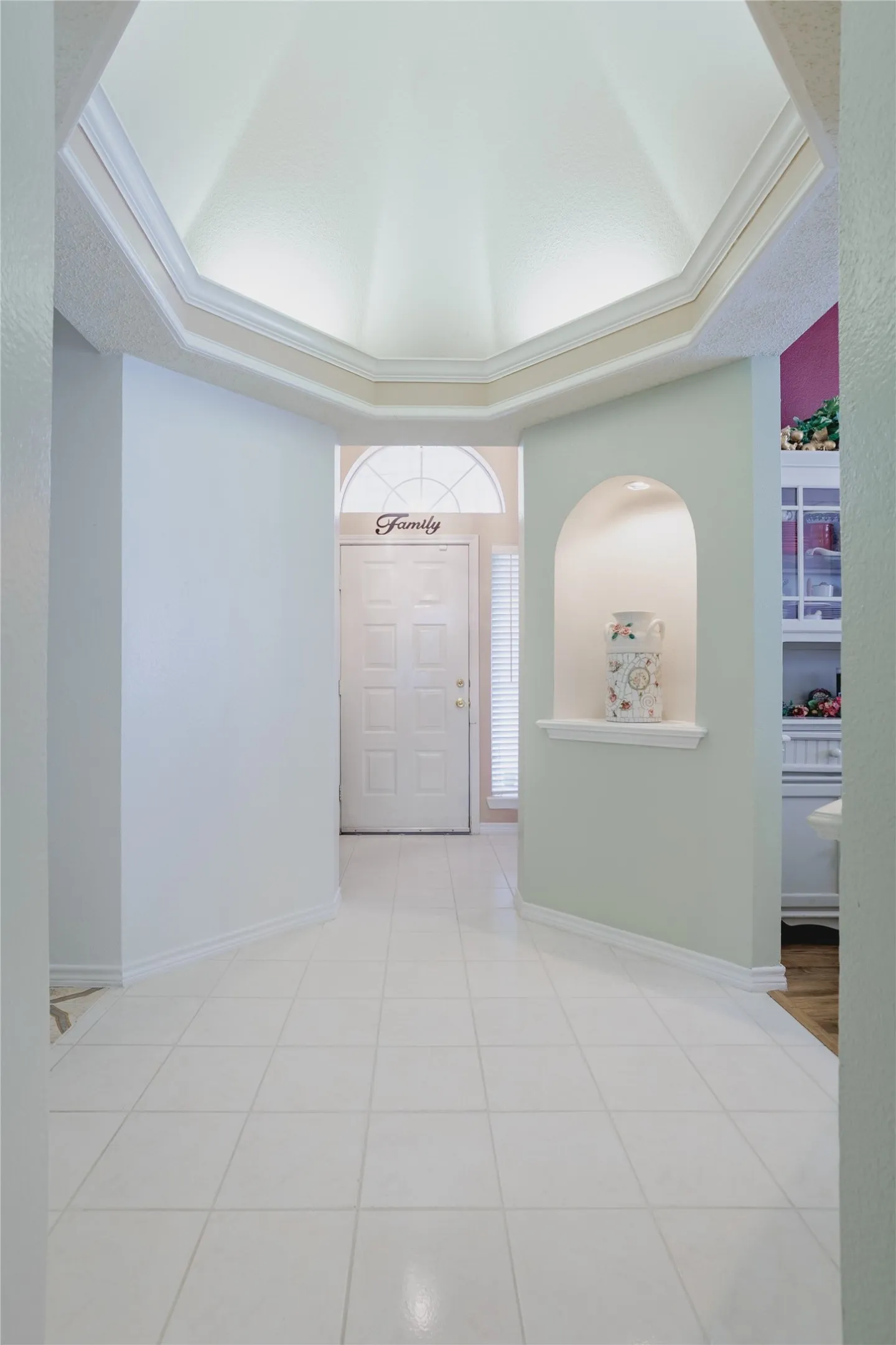Foyer featuring a domed ceiling with crown molding, light-toned tile flooring, and an arched wall niche with integrated shelf