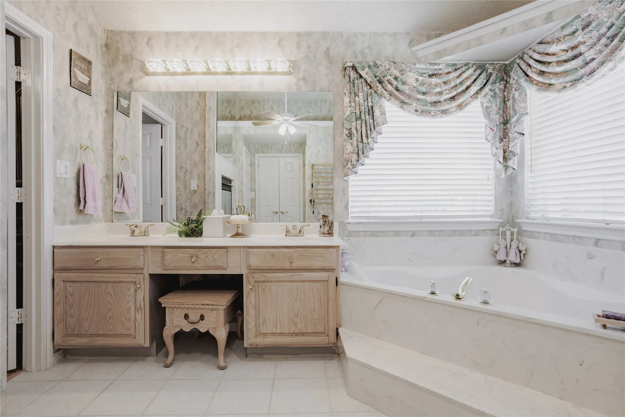 Dual vanity with integrated sinks, built-in cabinetry, large mirror, and full-size soaking tub with tiled surround