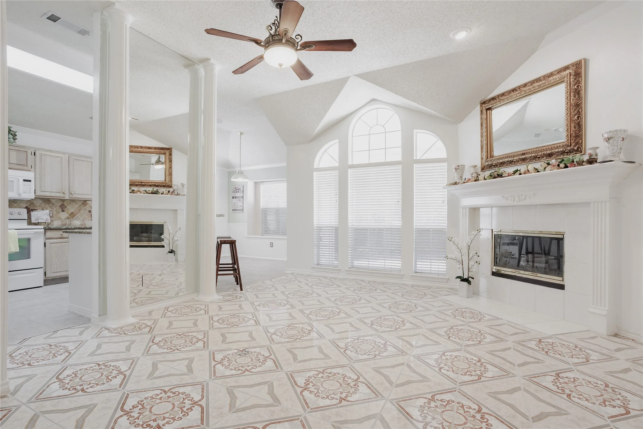 Vaulted ceilings with a ceiling fan, decorative tile flooring, arched windows, and a tiled fireplace with a mantel