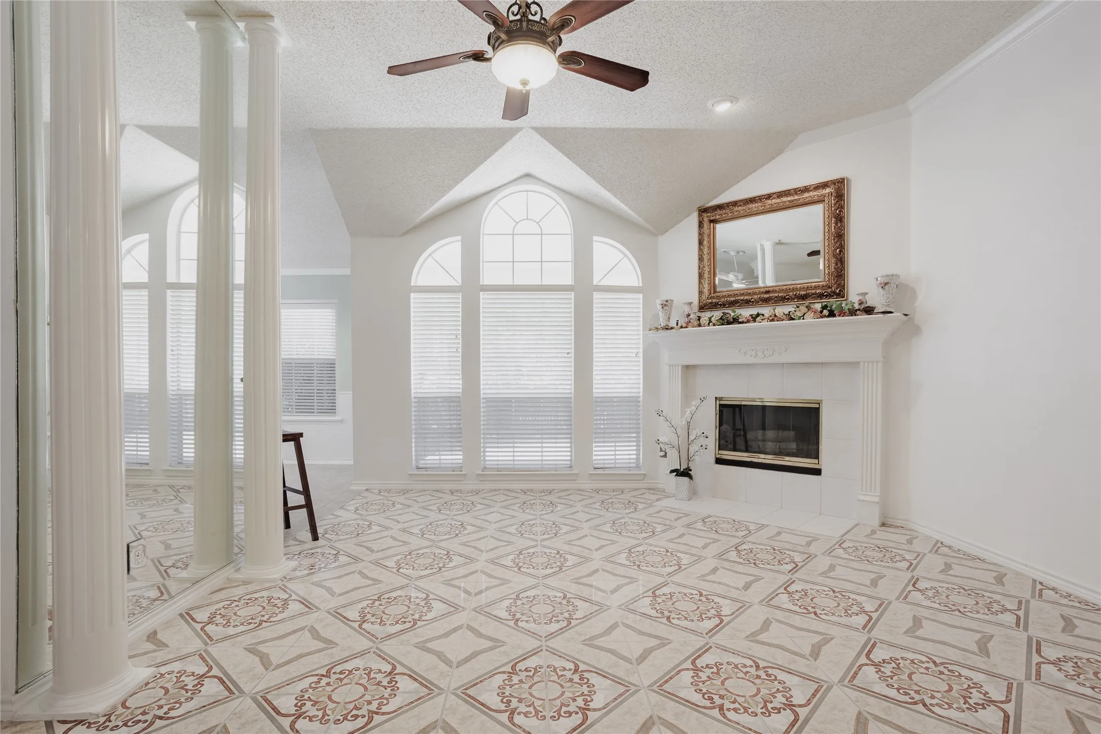 Vaulted ceiling with a ceiling fan, decorative tile flooring, arched windows with blinds, and a built-in fireplace with a mantel
