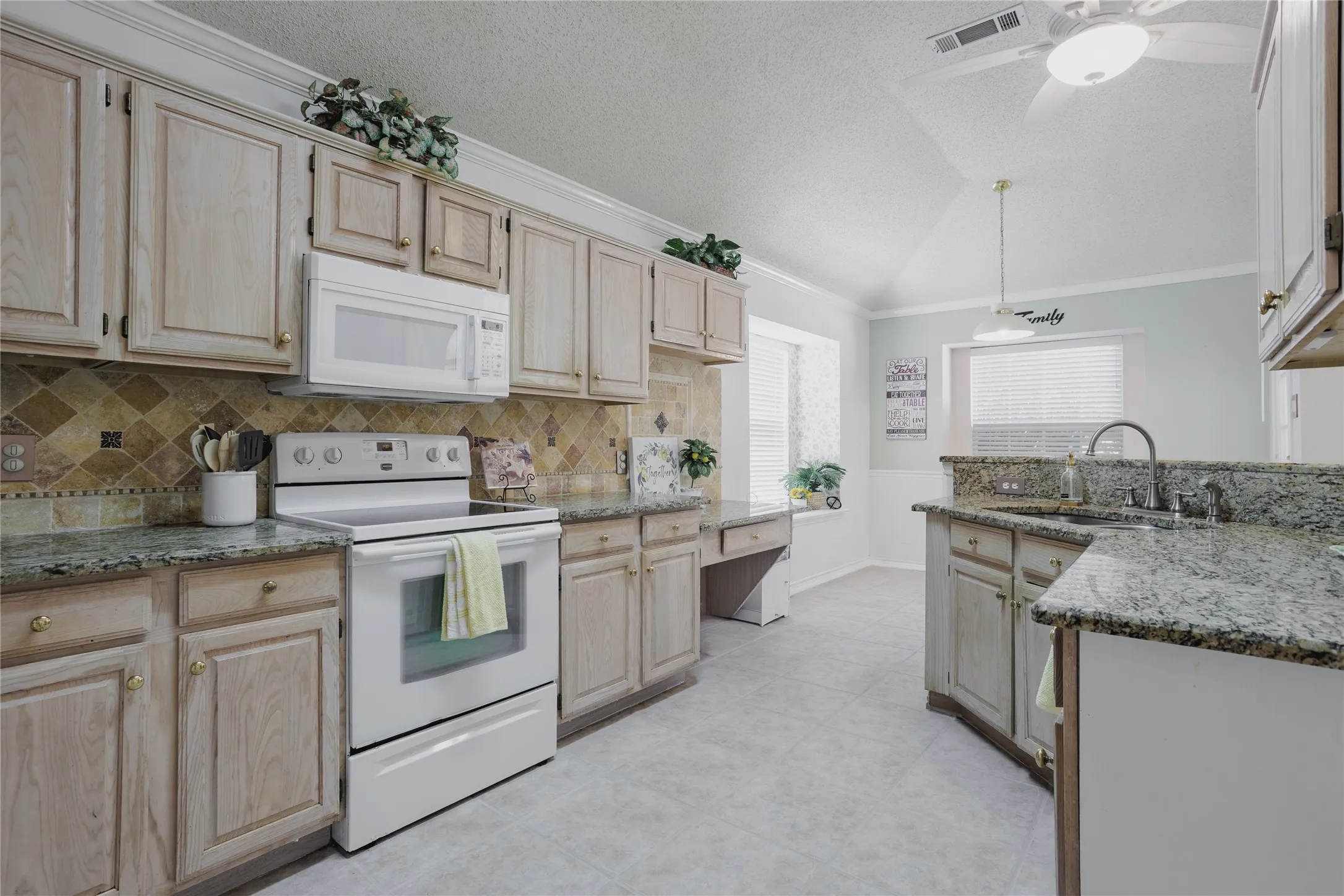 Vaulted ceiling, ceiling fan, built-in microwave, tile backsplash, and granite countertops