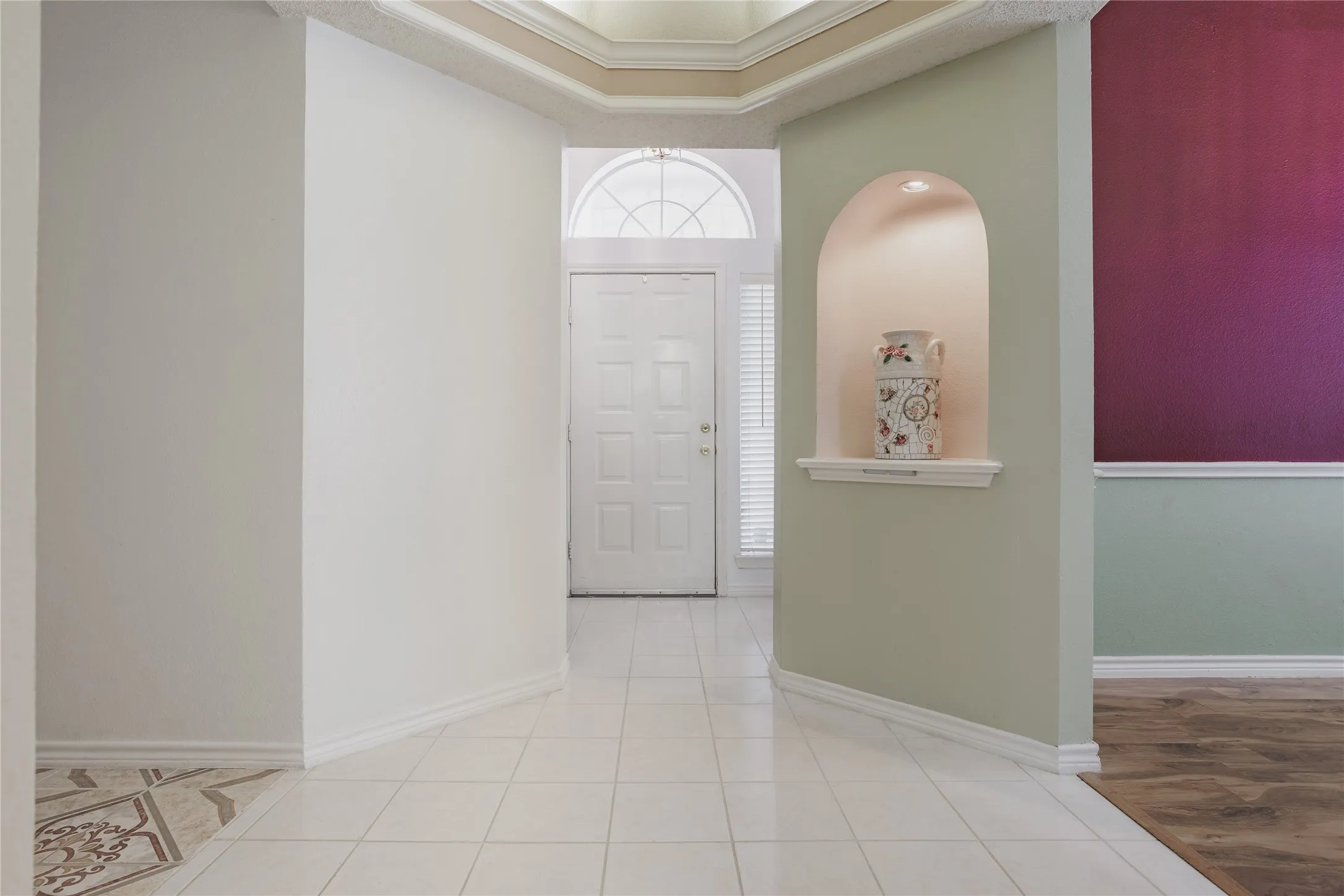 Elegant foyer showcasing neutral wall finishes, decorative arched niche with accent lighting, tile flooring, and refined crown molding detail