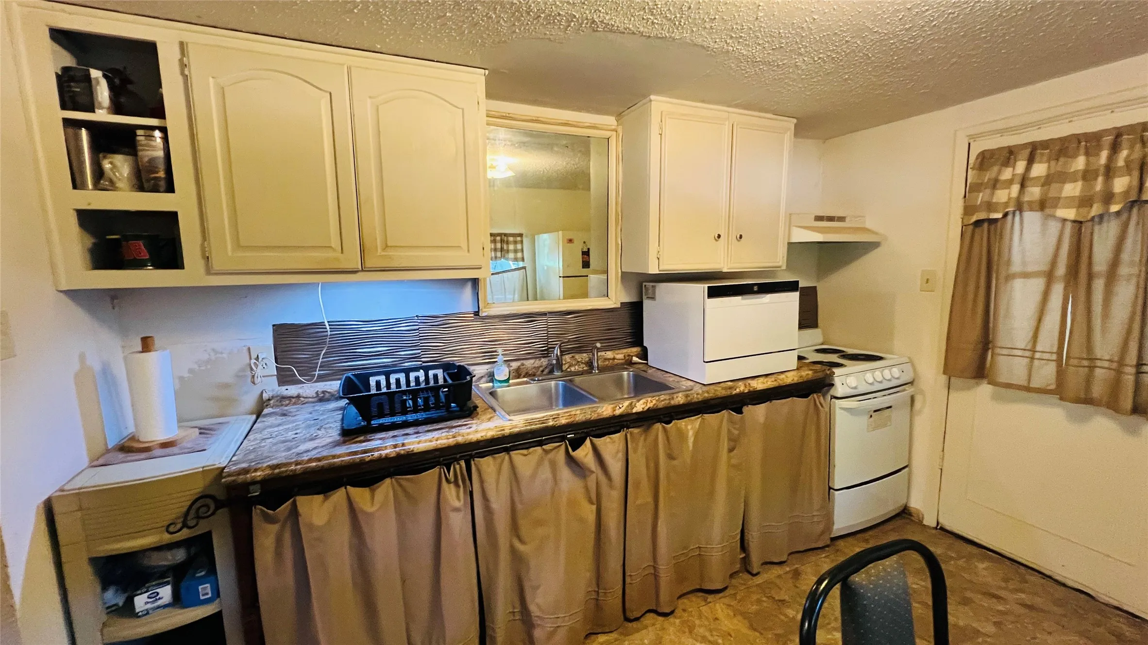 Kitchen with cream cabinetry, a double basin sink, and a white freestanding range, and back door accessing laundry room and to the backyard