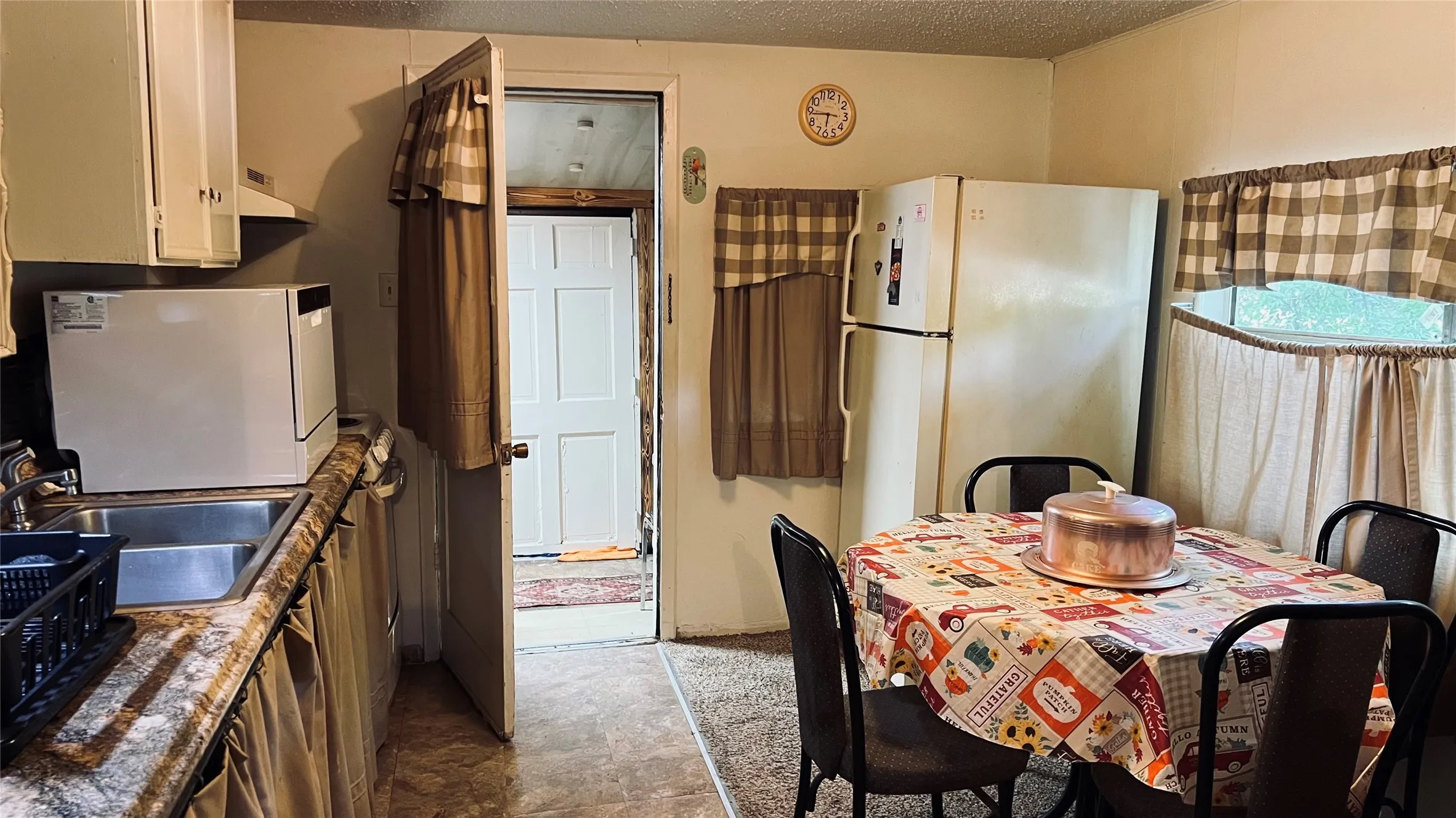 Kitchen featuring a double basin stainless steel sink, white upper cabinetry, and a laminate countertop with a stone finis, back door access to laundry room and backyard.  Ample natural light from large side window.