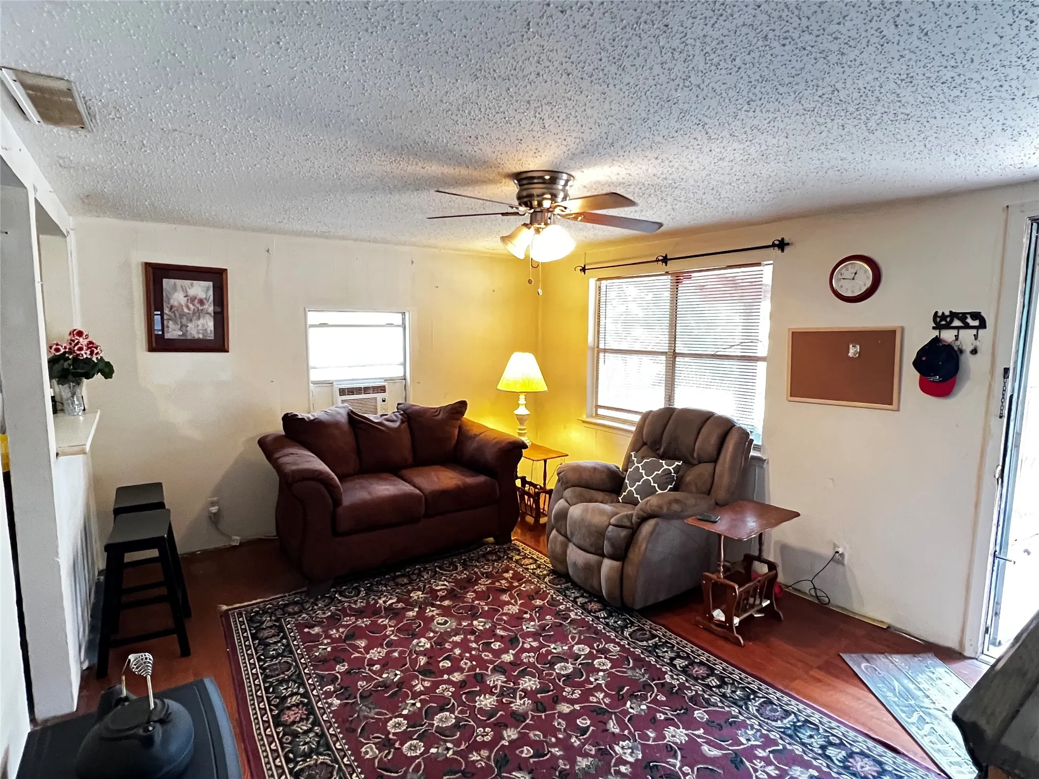 Living area featuring wood-finish flooring, a ceiling fan with integrated lighting, and multiple windows with valances providing ample natural light