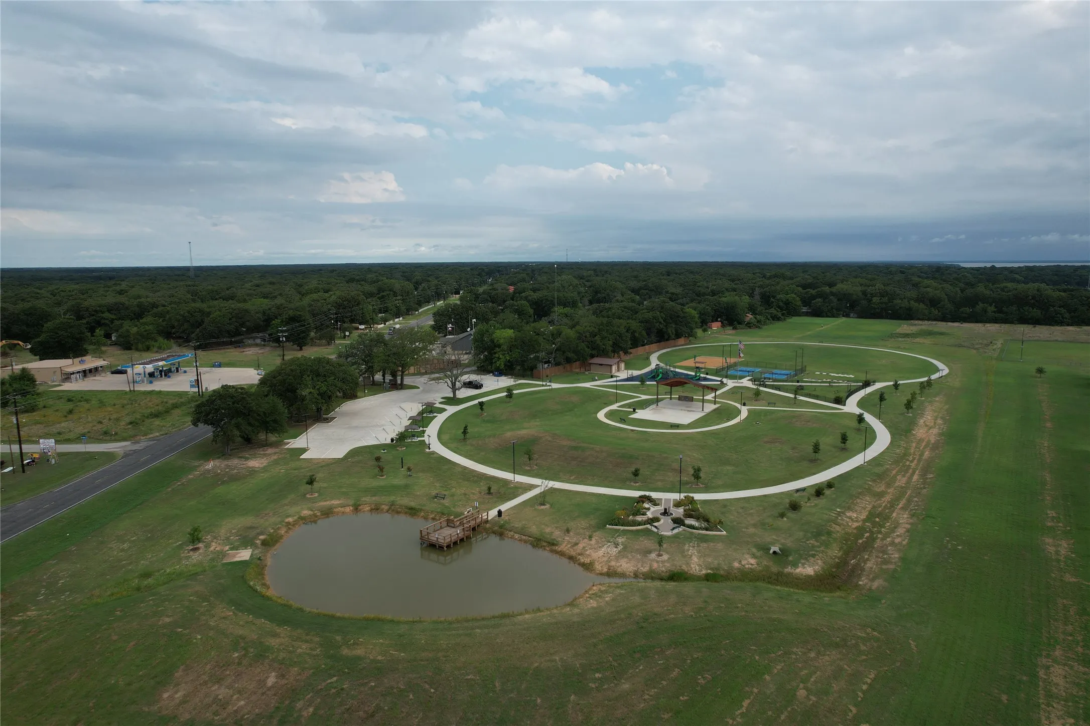 The Eight at Tool Park xpansive recreational grounds featuring a pond with a wooden dock, winding paved pathways, sports fields, and a covered pavilion